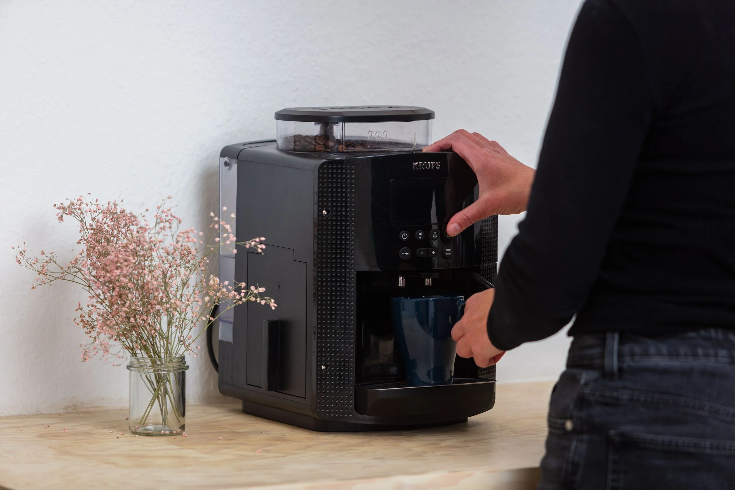 Auf dem Bild sieht man eine schwarze Kaffemaschine und eine Hand, die eine Tasse unter das Gerät hält.