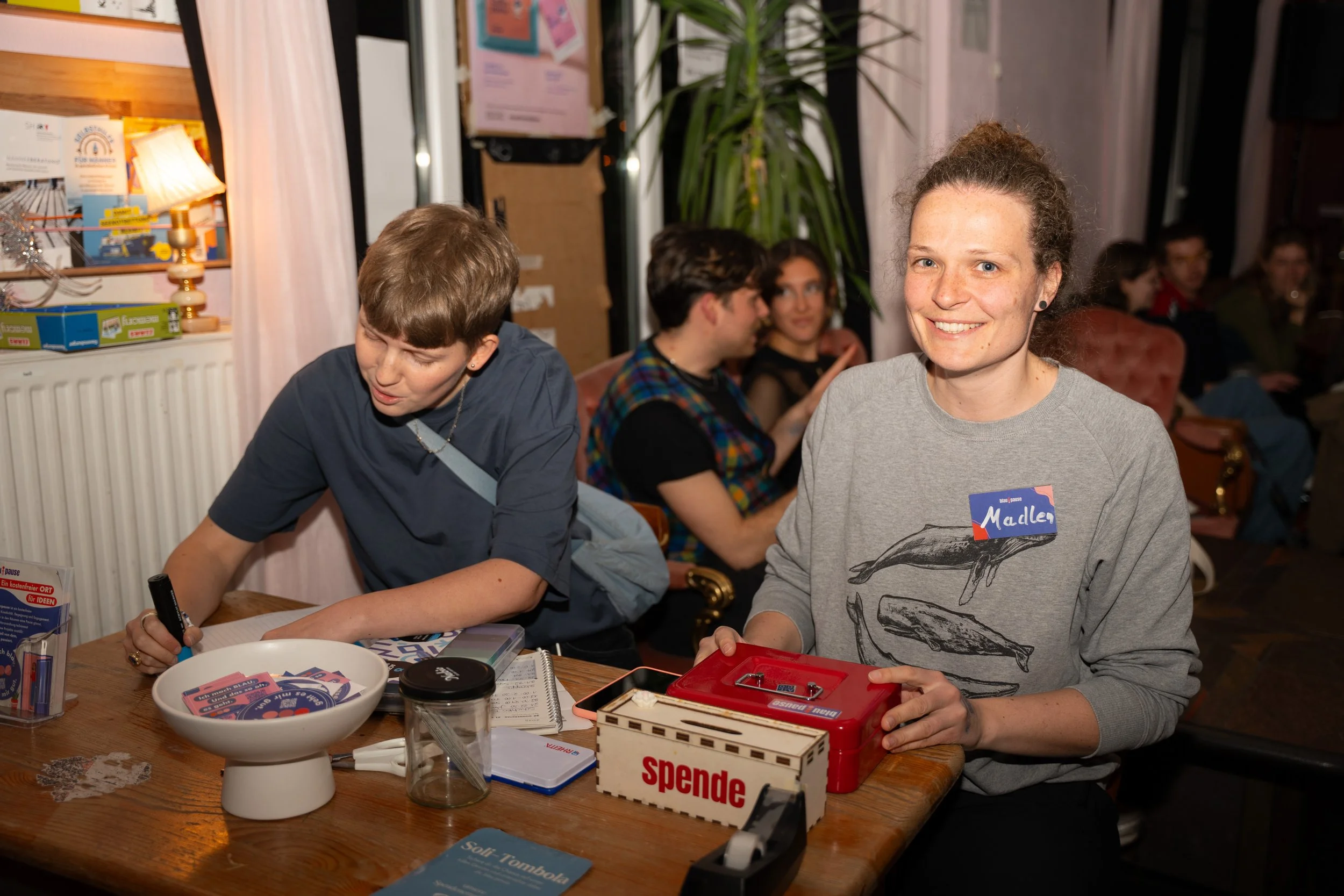 Auf dem Bild sieht man zwei Personen, die an einem Tisch sitzen. Sie sitzen am Eingang der Partylocation und machen den Einlass.