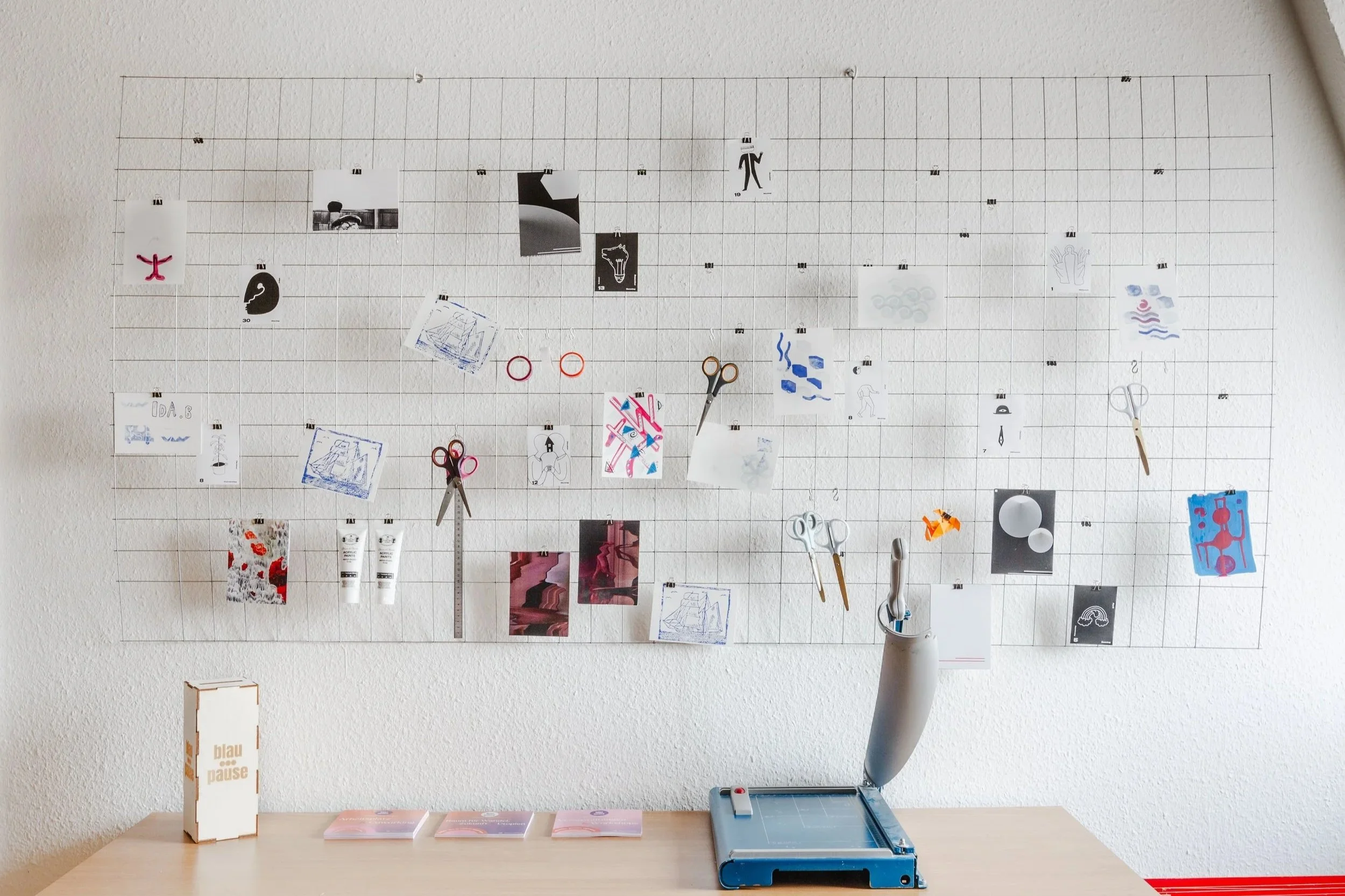 Man sieht ein Detailbild von einer Wand im kreativ:treff. Es hängen zwei Metallgitter an der Wand. An der Wand sind viele Flyer befestigt und kleine Bilder.