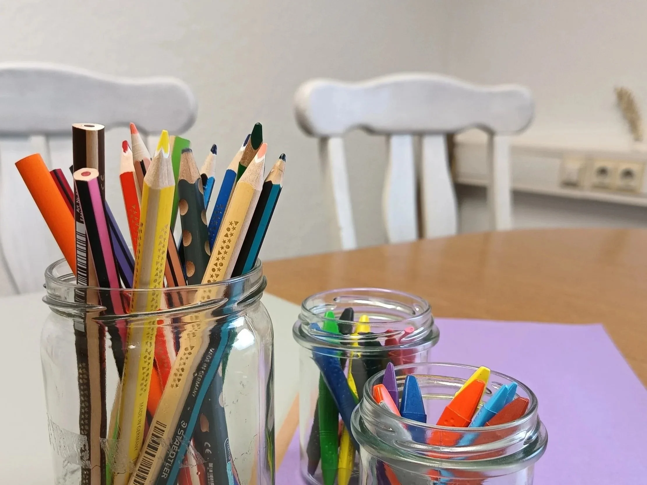 Man sieht einen Bildanschnitt von einem Tisch. Auf dem Tisch sind drei Gläser in denen viele bunte Stifte stecken.