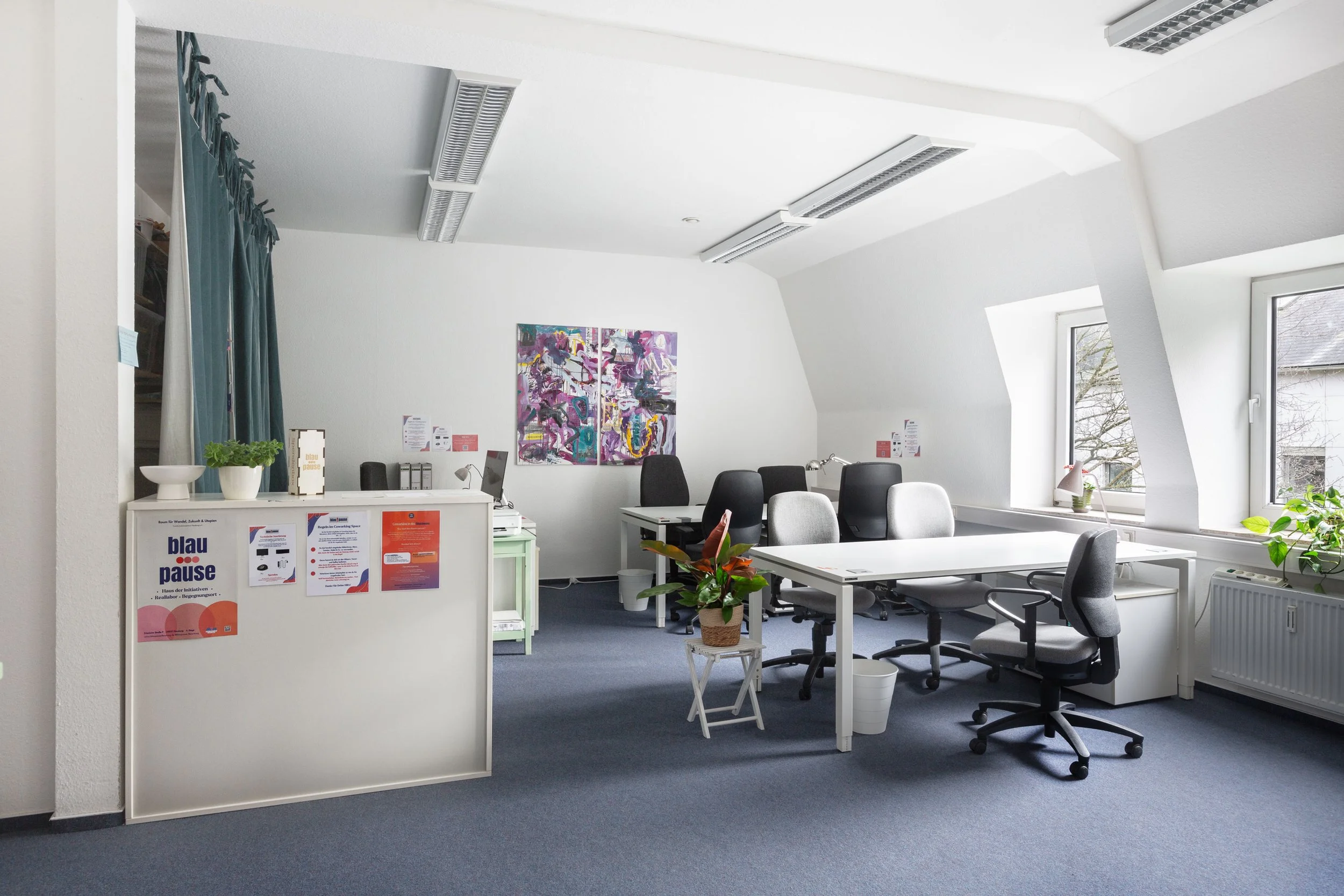 Auf dem Bild sieht man einen hellen großen Büroraum mit vielen Tischen und Stühlen. Im Vordergrund sieht man eine Art Tresen.