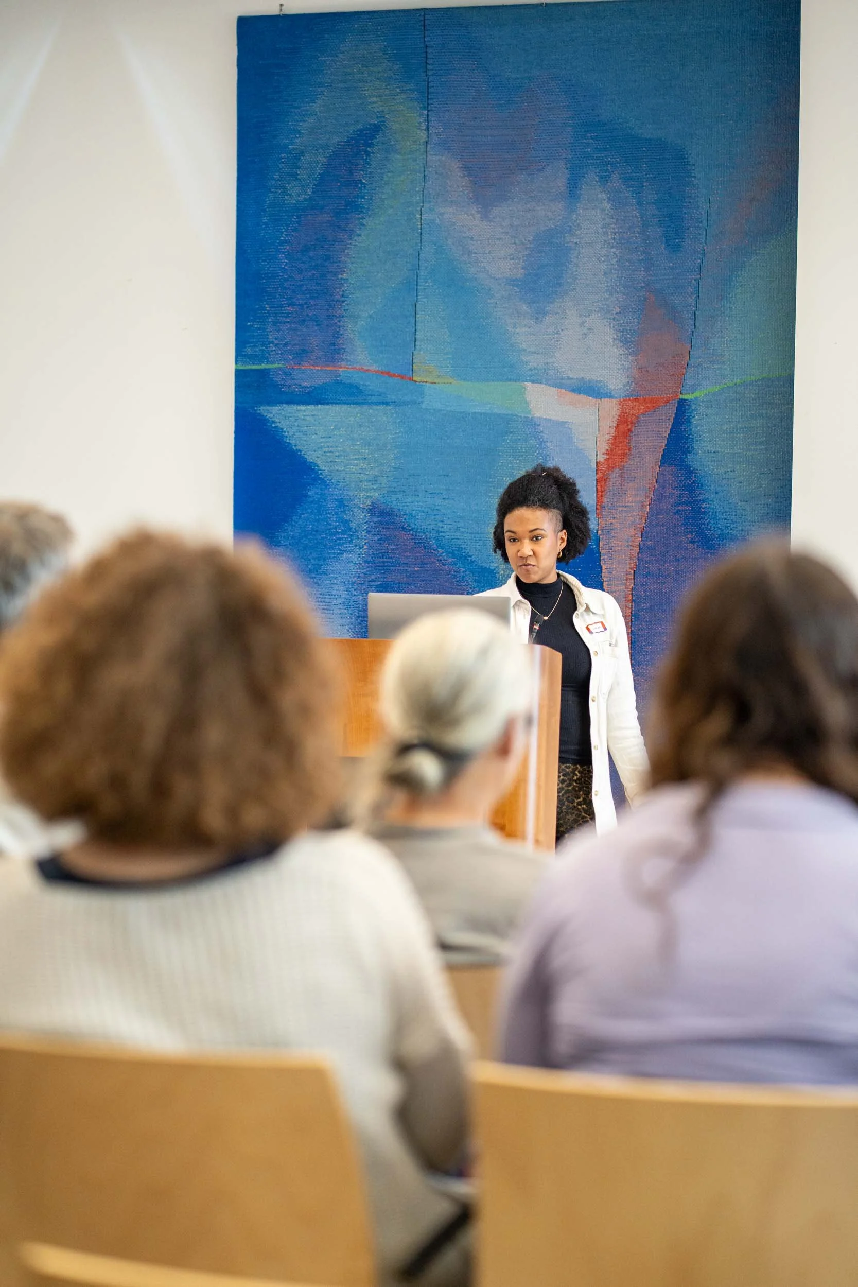 Auf dem Bild sieht man eine Person, die vor einer Menschenmenge einen Vortrag hält.