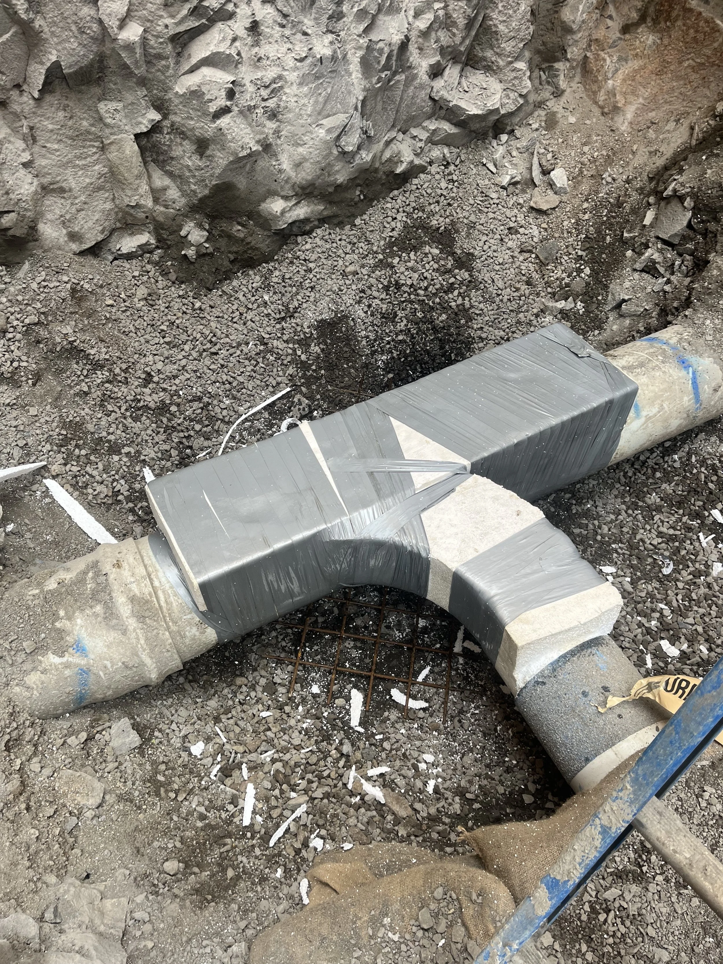 Underground pipe repair with gray duct tape wrapped around a broken pipe in a construction site.