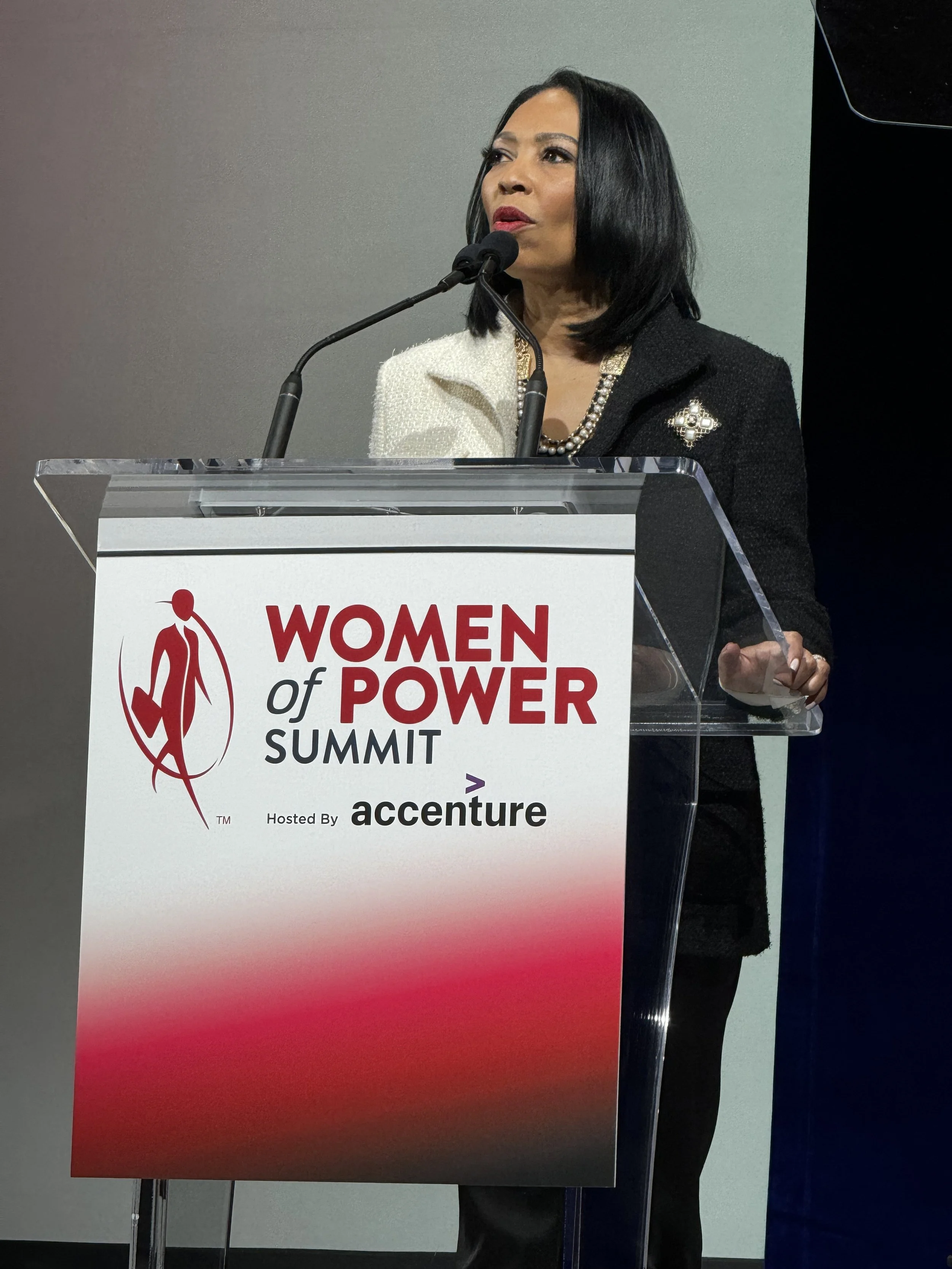 A woman with black hair speaking at a podium during a Women's Power Summit, hosted by Accenture.