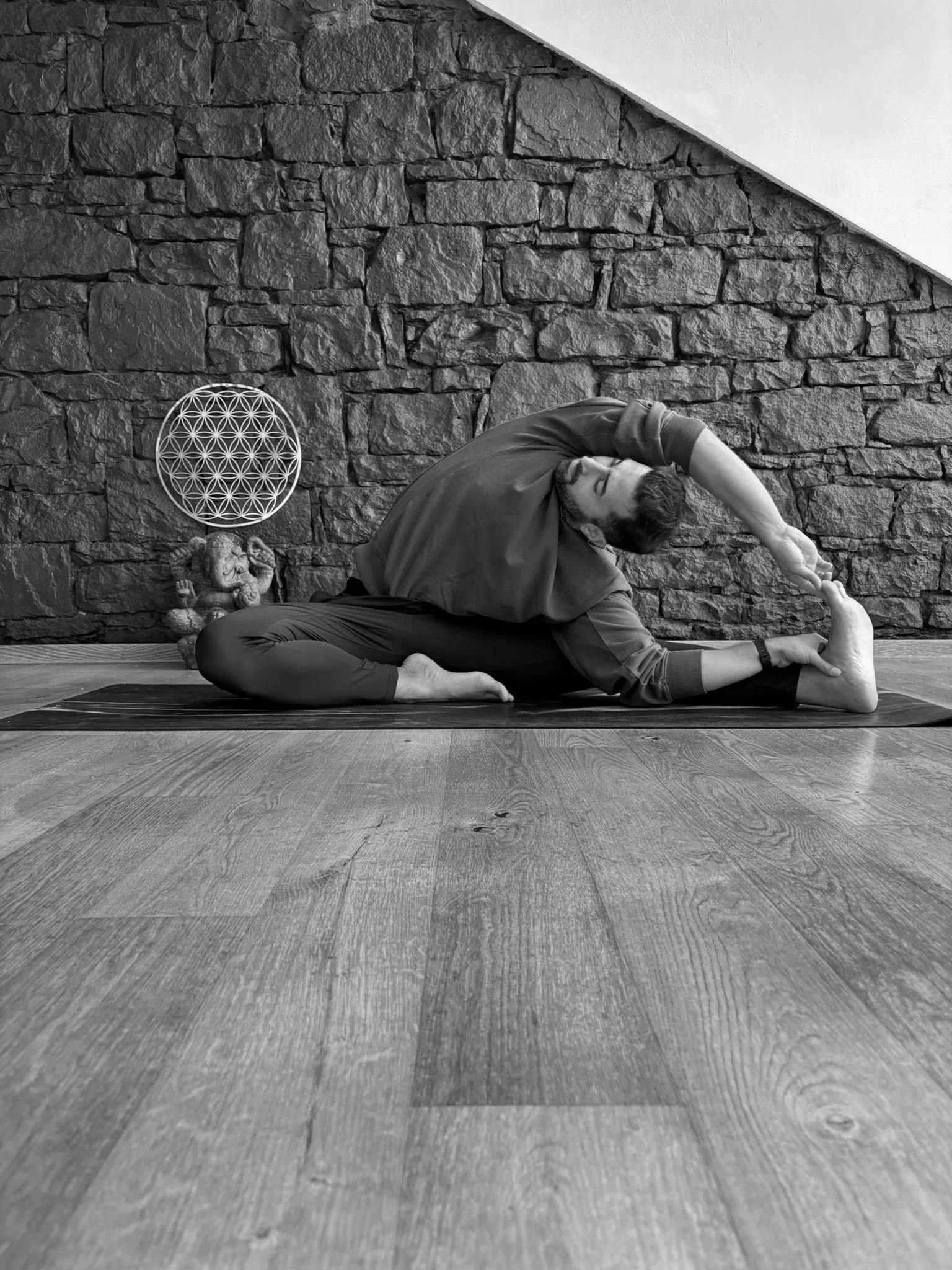 Mann macht Yoga auf einer Matte vor einer Steinwand in einem Raum mit Holzboden.