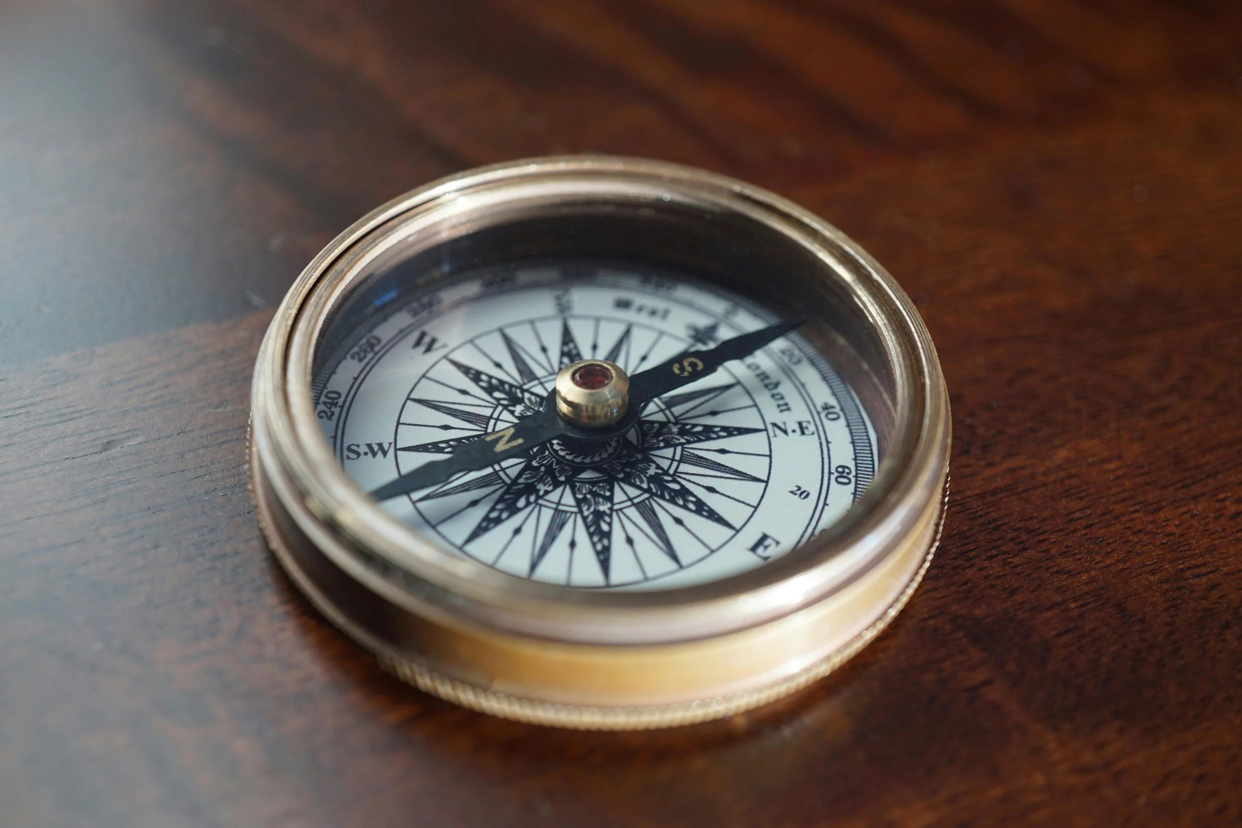 A vintage brass compass with a glass cover resting on a wooden surface.