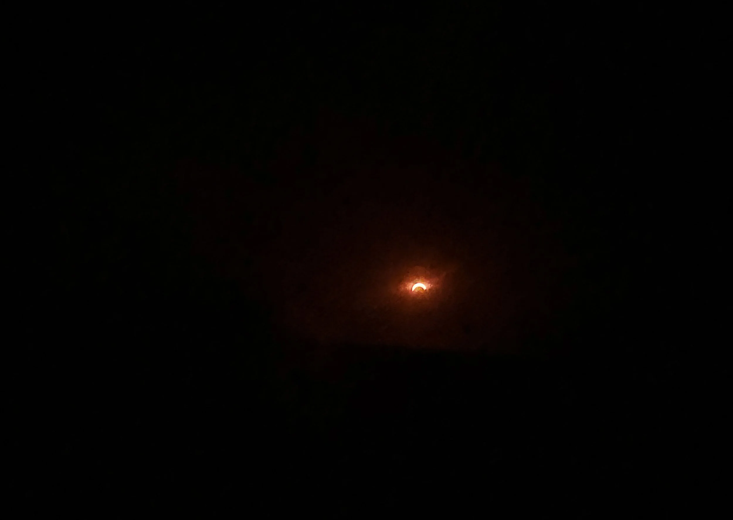 A lunar eclipse occurring at night with the moon partially obscured, glowing red against a dark sky.
