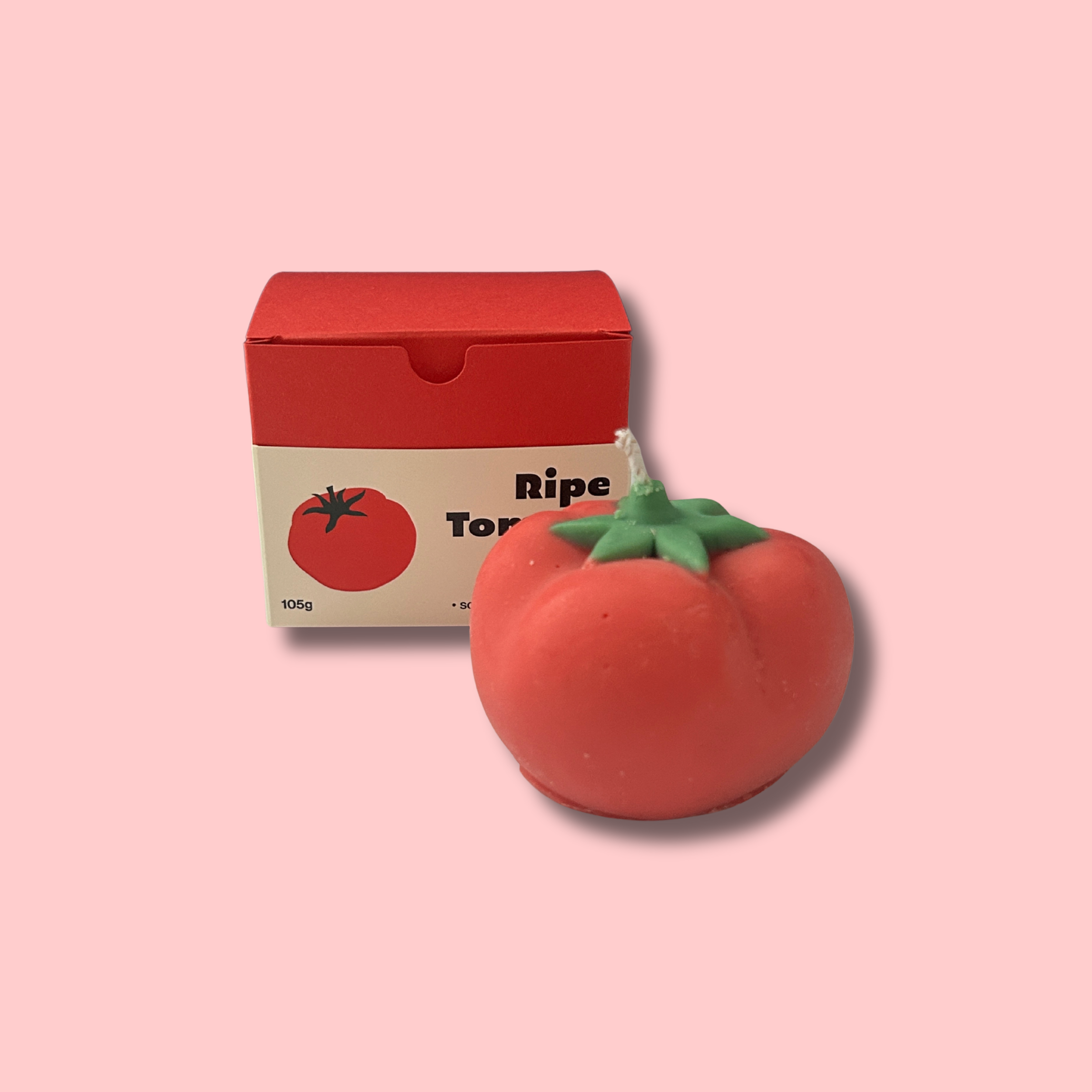 A decorative candle shaped like a ripe tomato next to a small box labeled "Ripe Tomato" with a tomato illustration on a pink background.