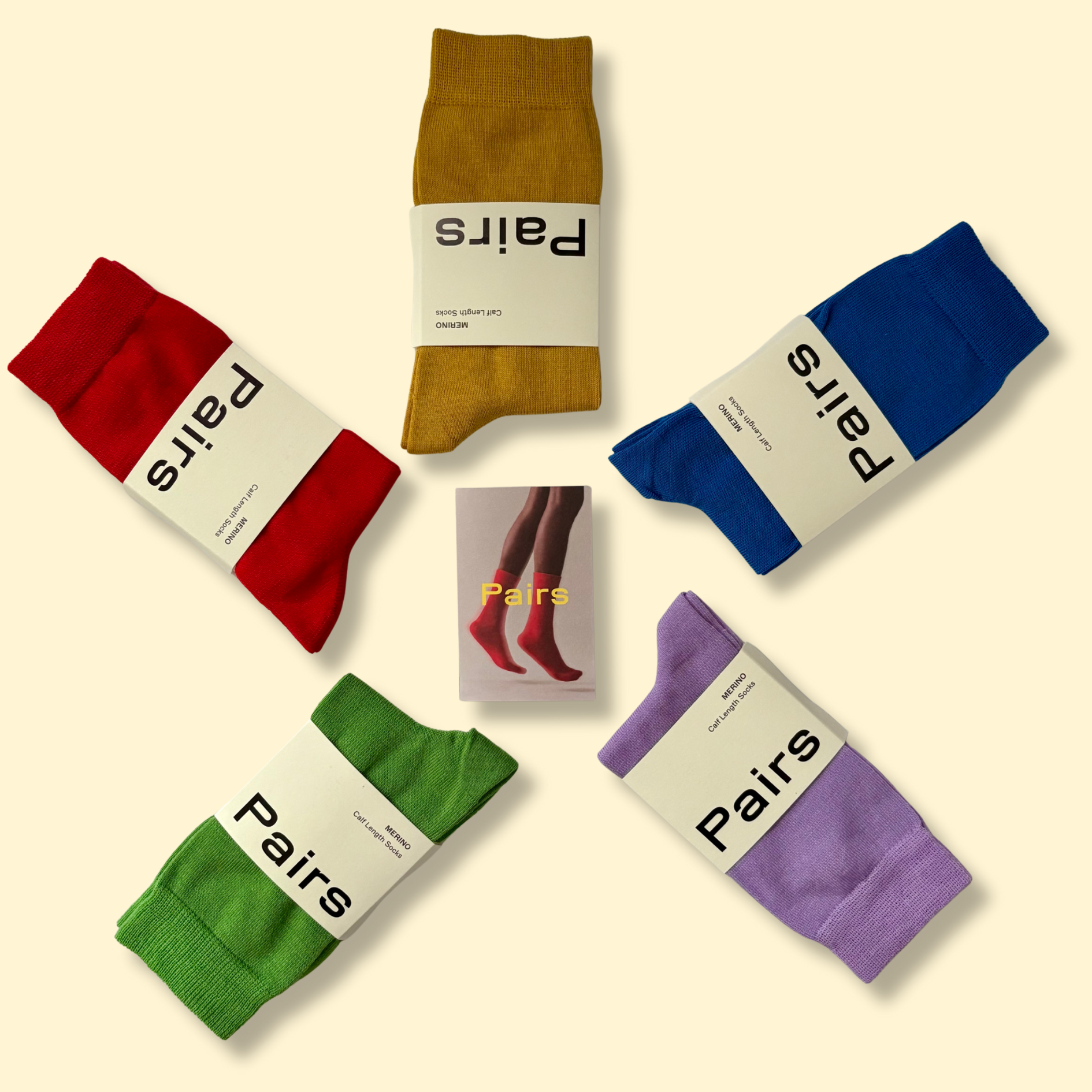 Colourful pairs of socks in red, yellow, blue, green, and purple arranged in a circle with a small card in the center showing legs wearing red socks and the word "Pairs".
