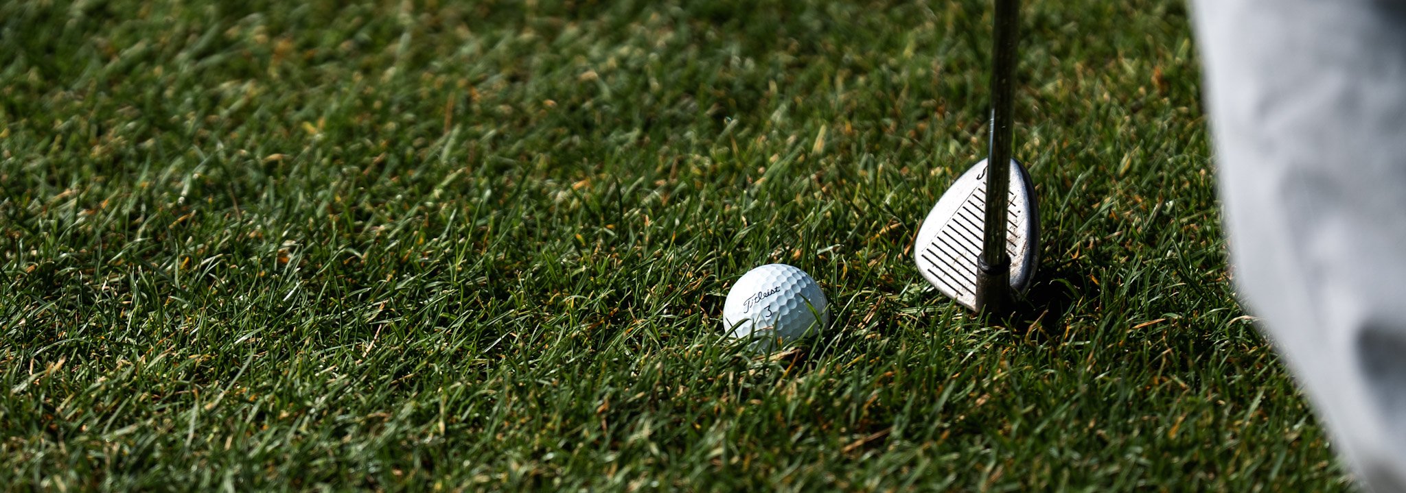 Close-Up Golf-Ball auf grünem Rasen mit Golfschläger daneben
