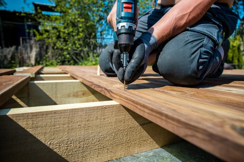 Carpenter installing timber decking using power tools on site