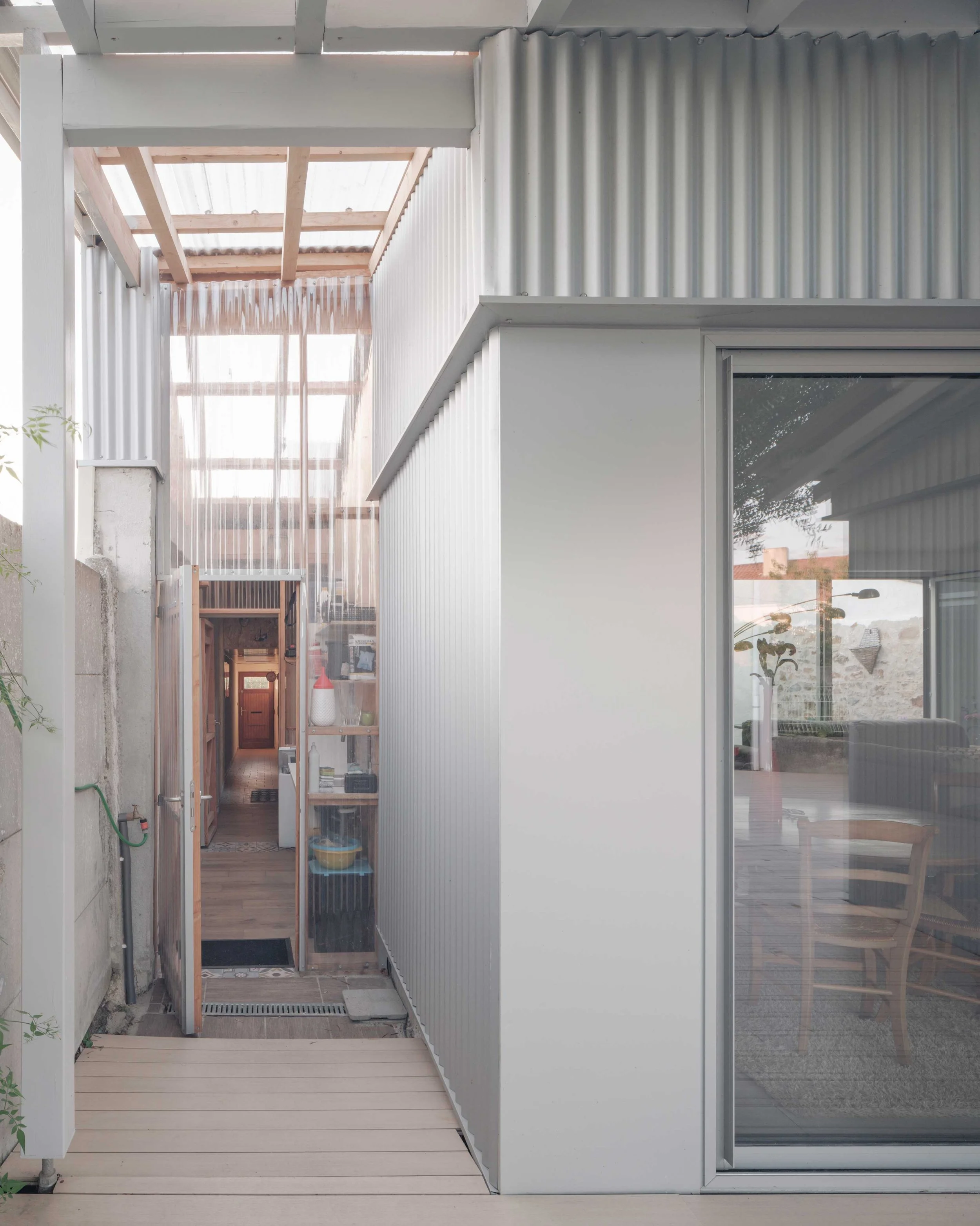 vue intérieur d'une maison moderne avec terrasse en bois, mur en métal ondulé, porte vitrée et mobilier.