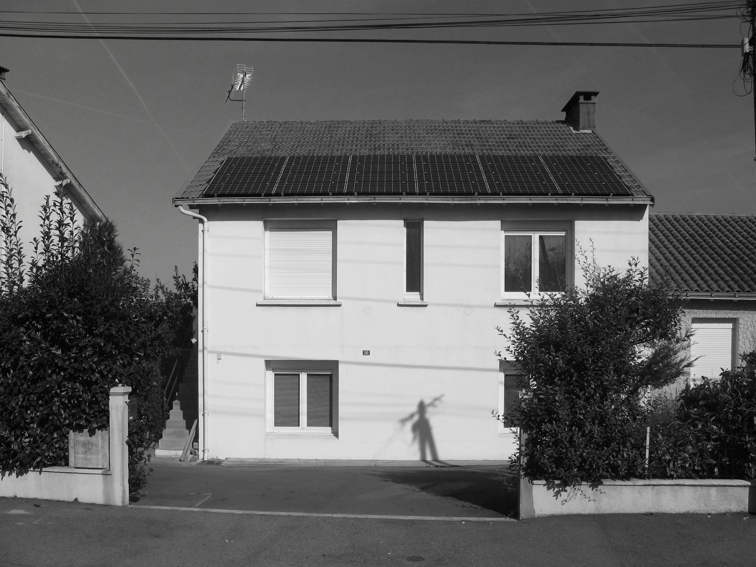 Une maison avec des panneaux solaires sur le toit, entourée d'arbustes, en noir et blanc.