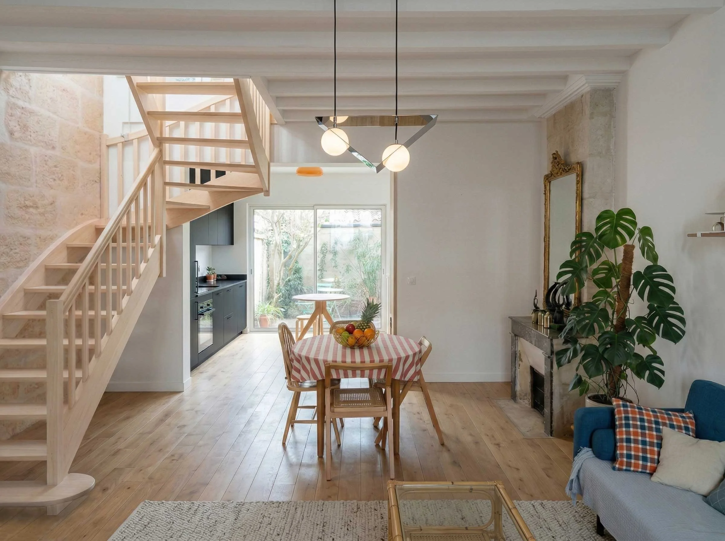 Intérieur d'une salle à manger et d'un salon avec un mobilier en bois, un lampadaire moderne, une plante verte et une cheminée en pierre.