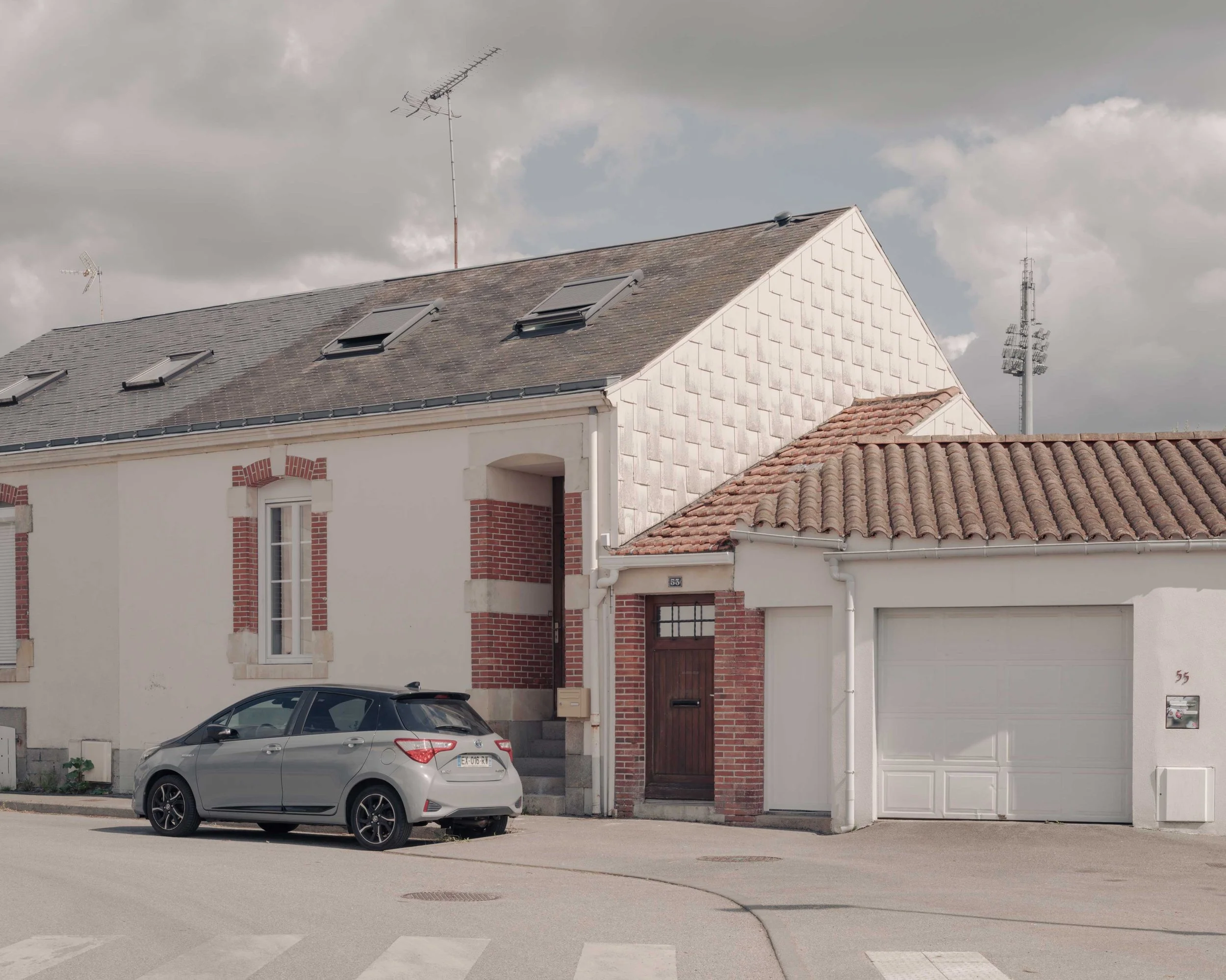Façade de maisons résidentielles avec des toits en tuiles, fenêtres de toit, antennes et un véhicule stationné devant l'entrée de la maison.