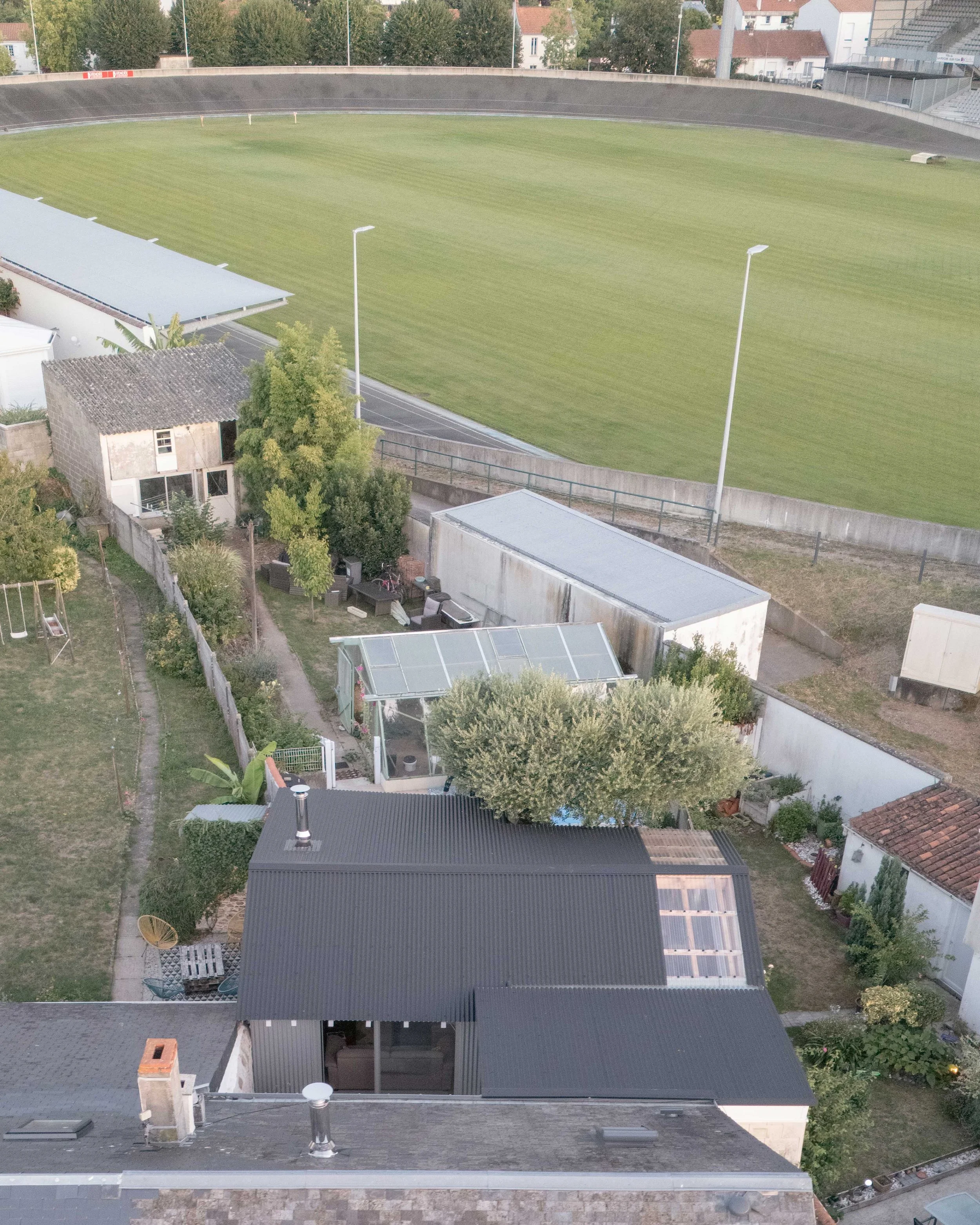 Vue aérienne d'un quartier résidentiel avec un terrain de sport ovale en herbe, entouré de bâtiments résidentiels et de jardins.