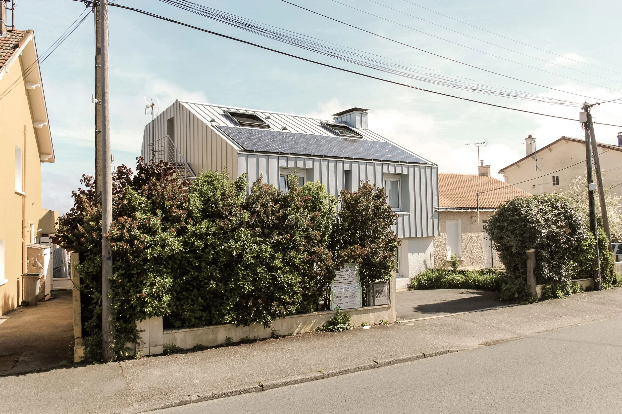 Une maison moderne avec des panneaux solaires sur le toit, entourée d'arbustes, dans un quartier résidentiel ensoleillé