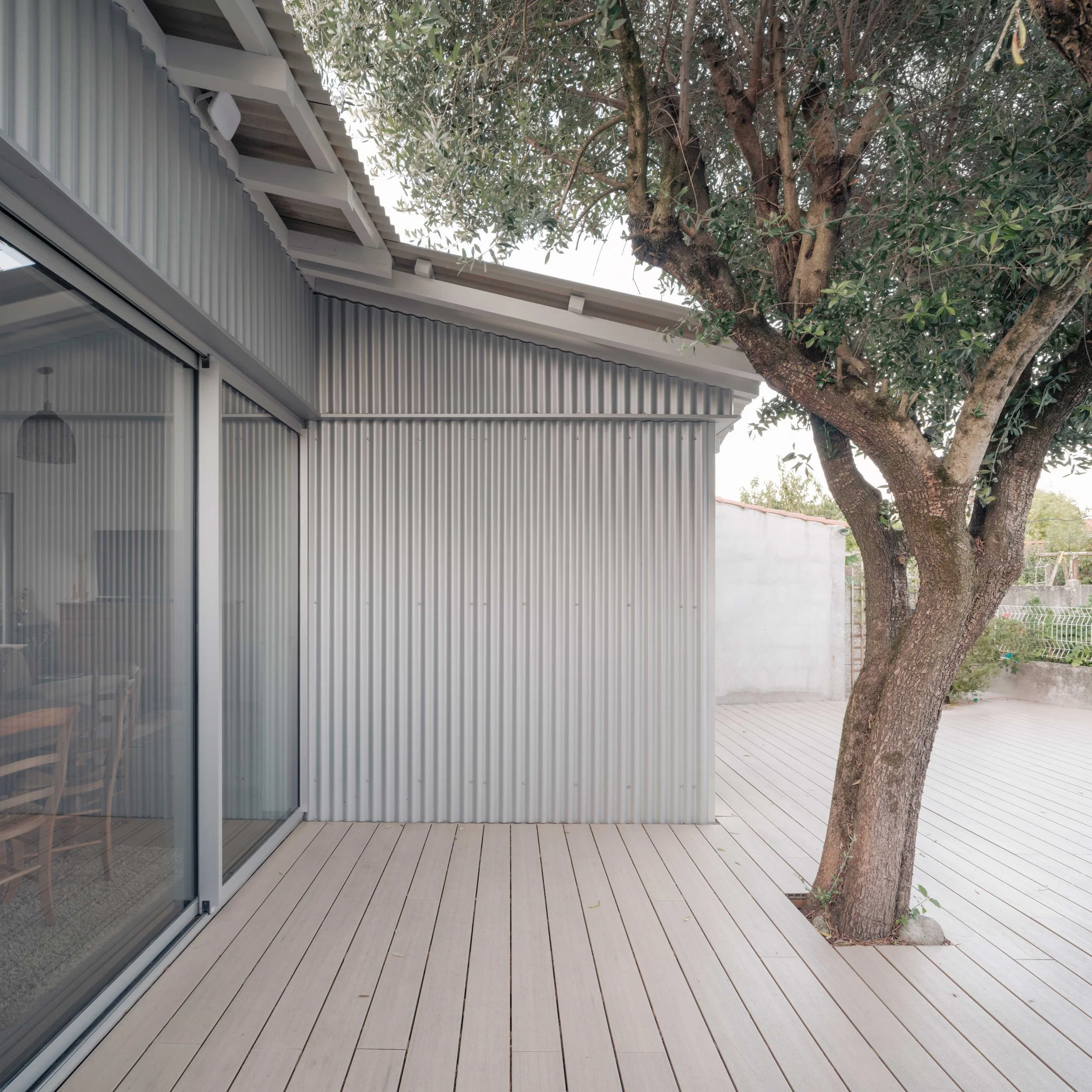 Terrasse en bois attenante à une maison en métal avec un arbre à proximité, vue depuis la terrasse.