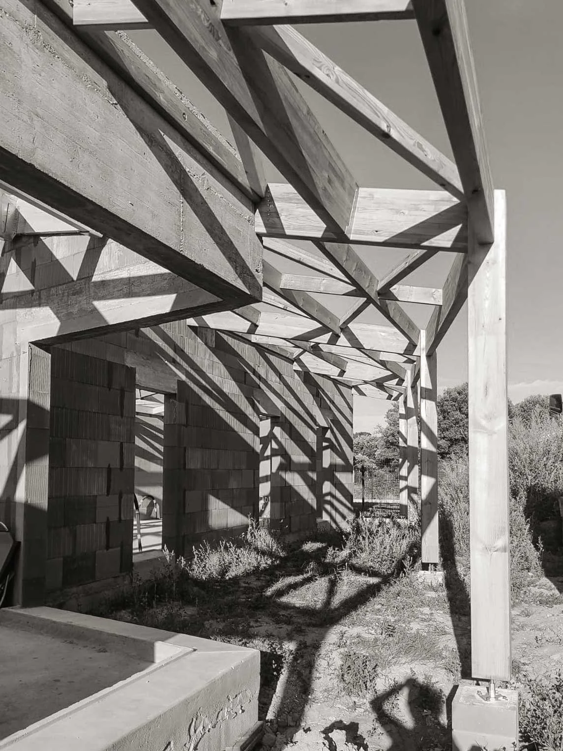 Structure de bois en construction avec des poutres et des ombres sur le sol, dans un endroit en plein air.
