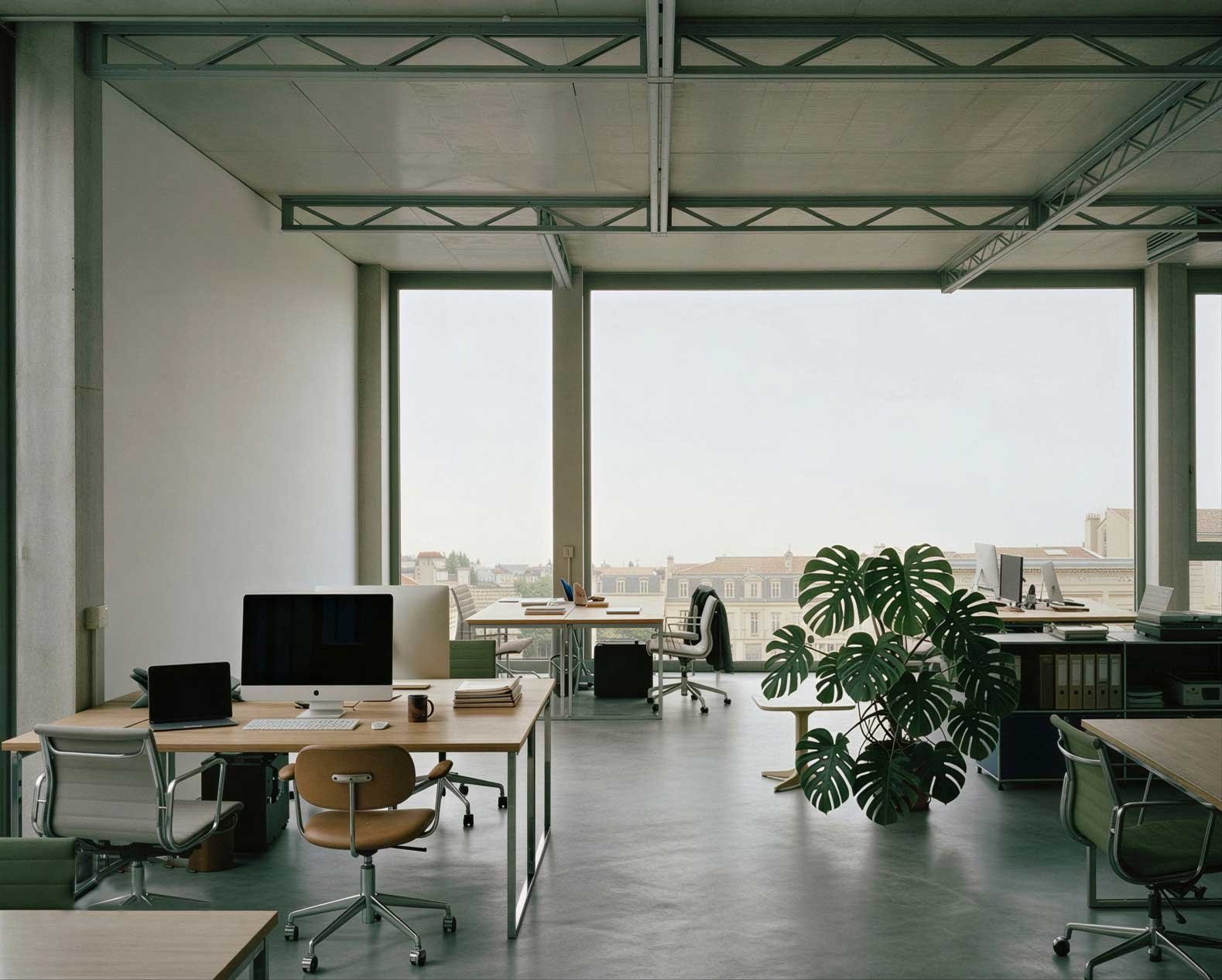 Bureau moderne avec plusieurs espaces de travail, ordinateurs, chaises, une grande plante verte, vue sur la ville par la fenêtre.