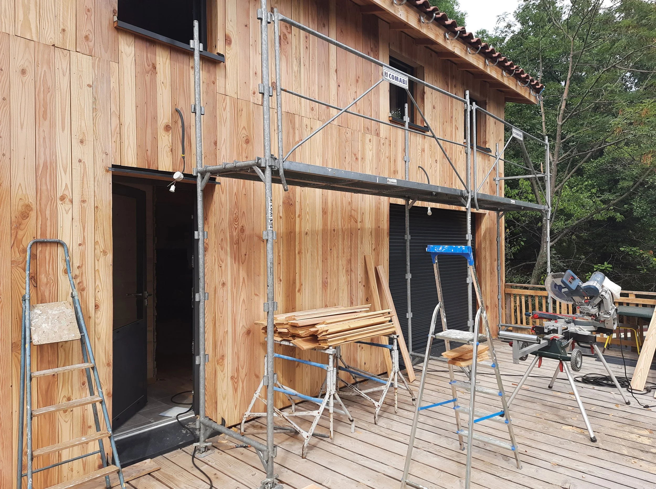 Une maison en construction avec un revêtement en bois, des échafaudages, des outils de menuiserie et des matériaux de construction sur un pont en bois.