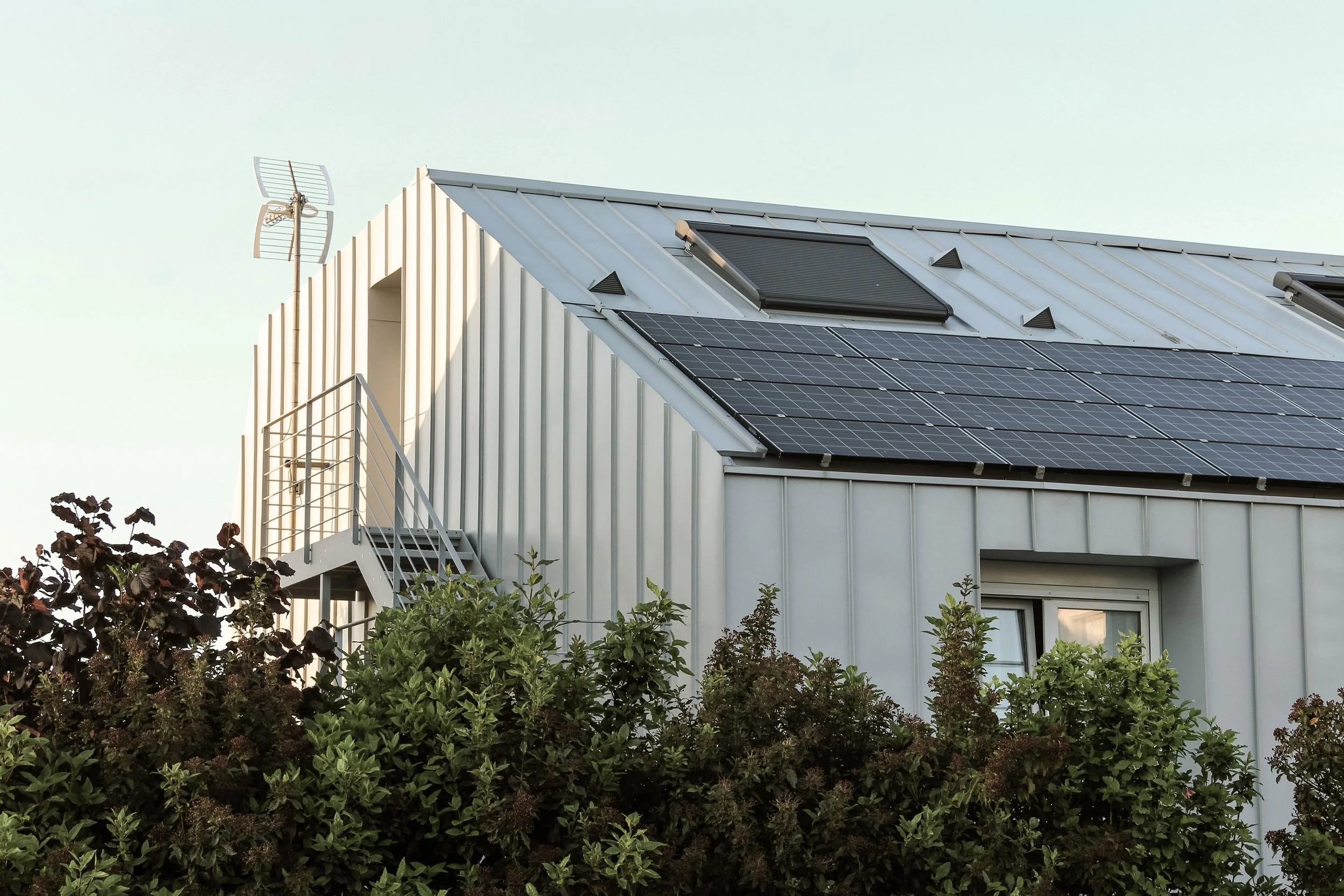Une maison avec des panneaux solaires sur le toit et un système d'antenne à l'extérieur, entourée de végétation.
