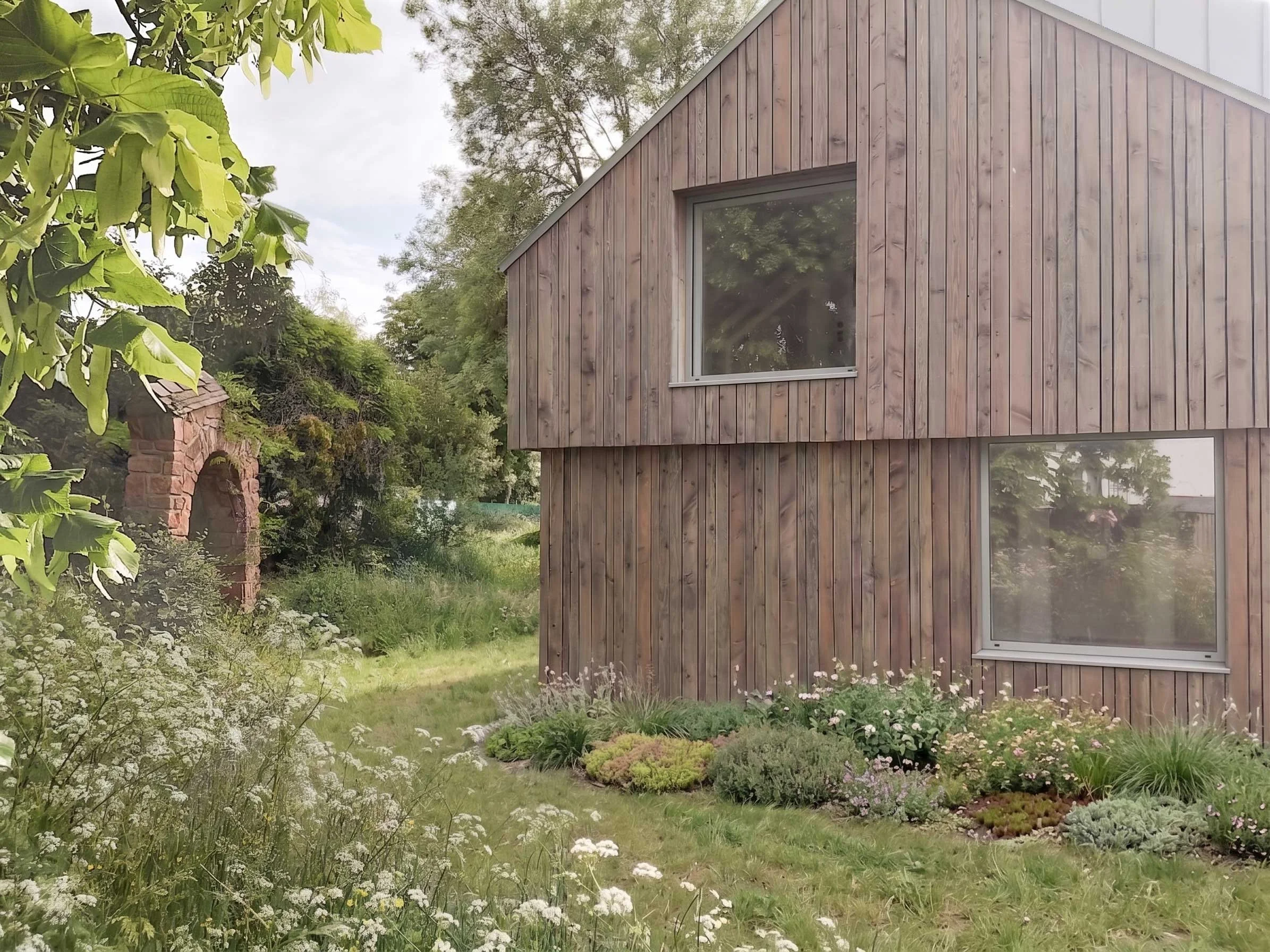 Une maison moderne en bois avec un toit en zinc, entourée d'un jardin verdoyant.