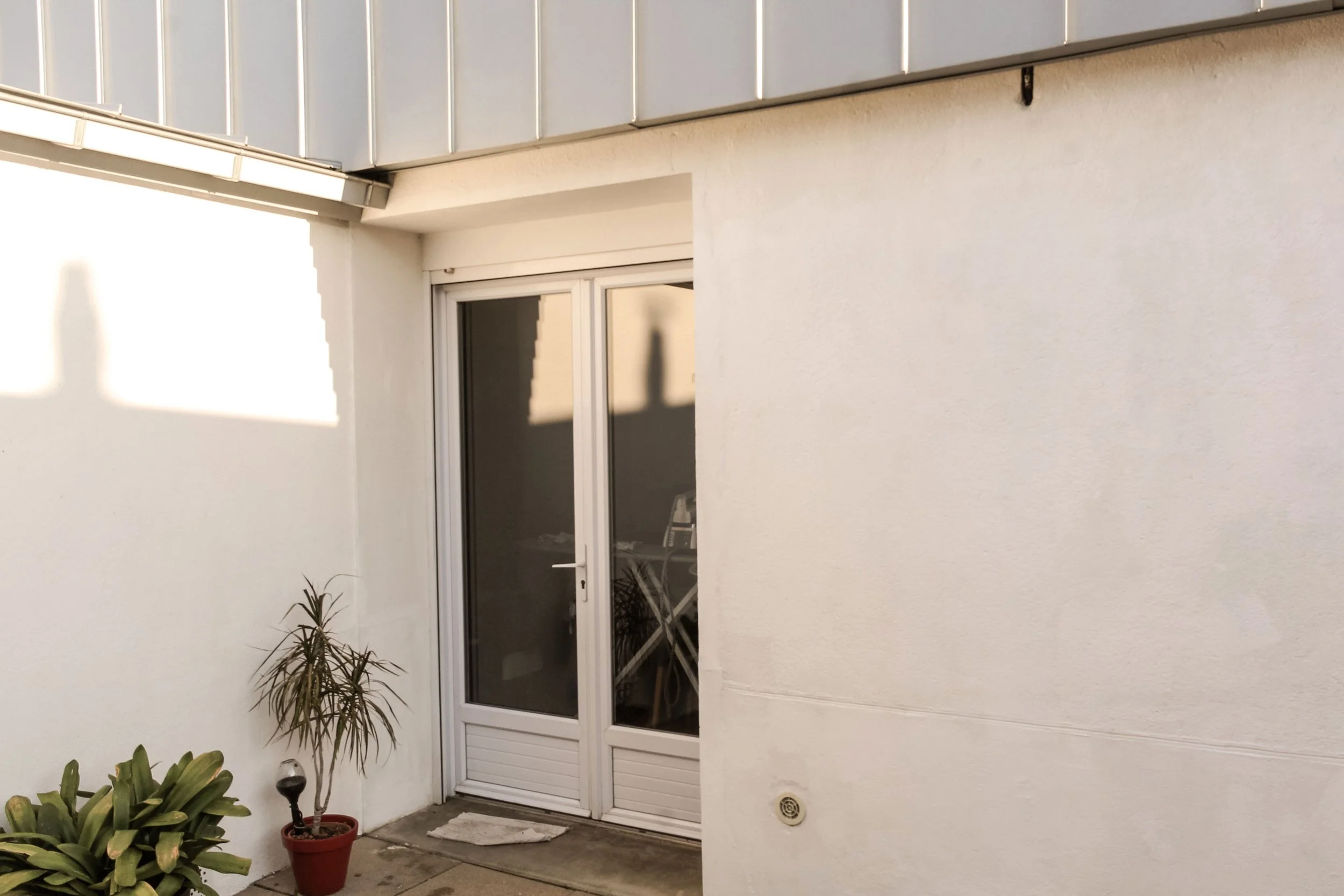 Balcon ou terrasse avec porte-fenêtre, plantes en pot et sol en béton