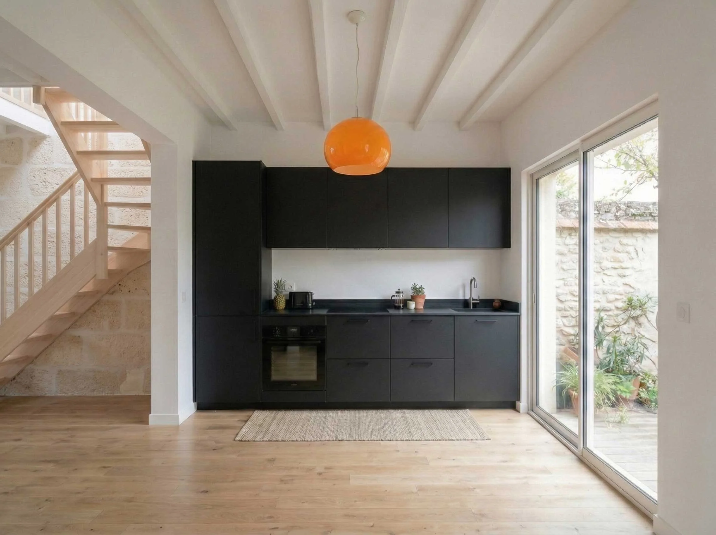 Intérieur moderne avec cuisine noire, grande fenêtre en verre, plancher en bois, plante, et suspension orange.