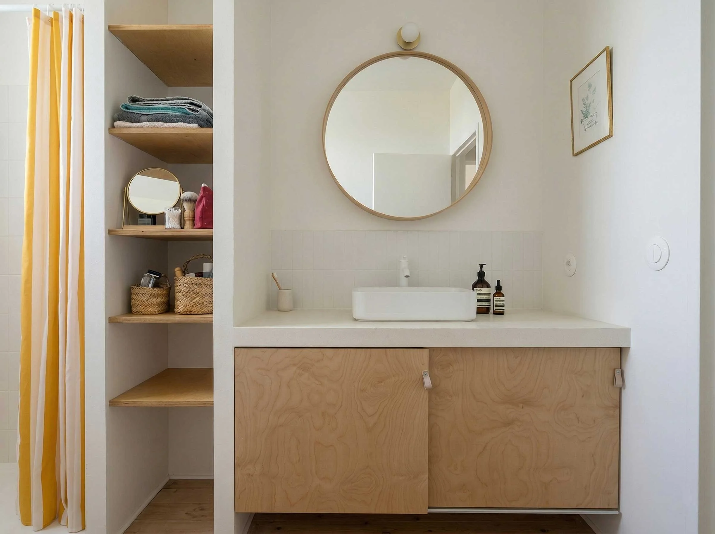 Un miroir rond au-dessus d'un lavabo dans une salle de bain moderne avec des étagères en bois contenant des serviettes et des accessoires de toilette.