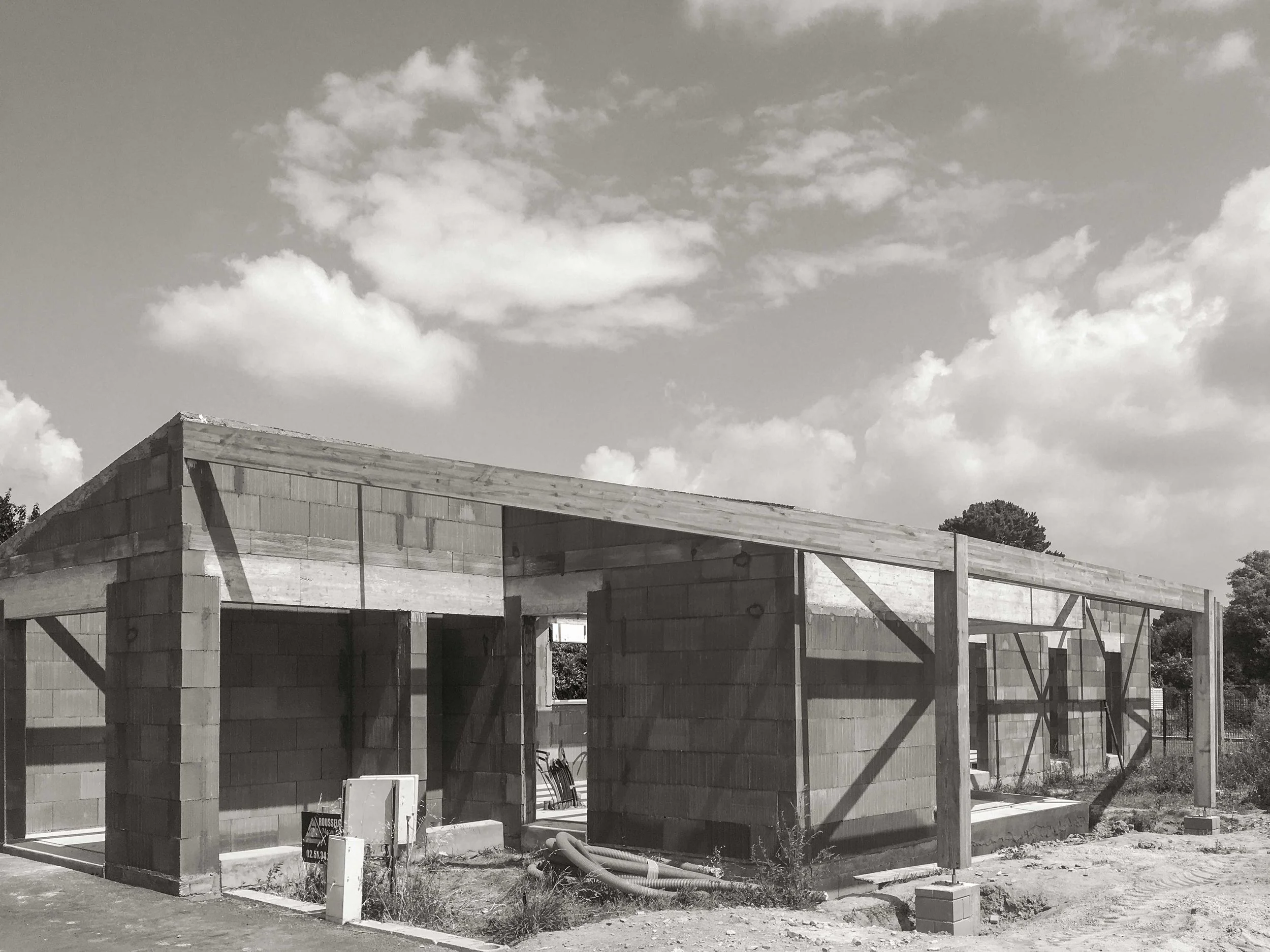 Une maison en construction avec des murs en blocs de béton et une charpente en bois, ciel nuageux en arrière-plan.