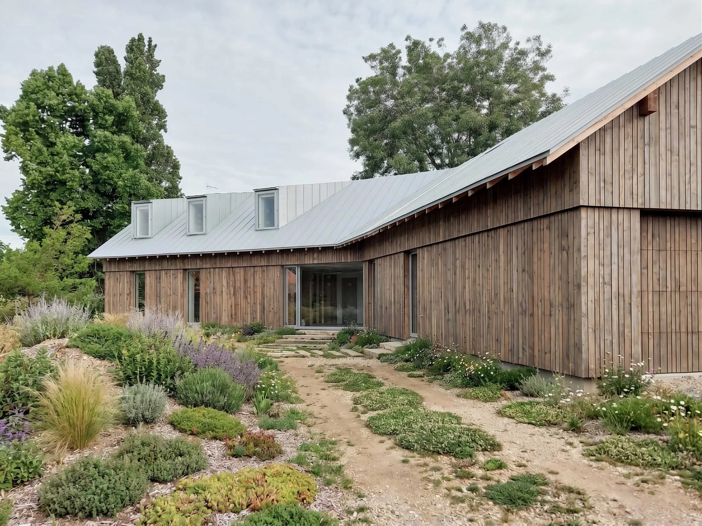 Une maison moderne en bois avec un toit en métal, entourée de jardin avec des arbustes et des arbres.