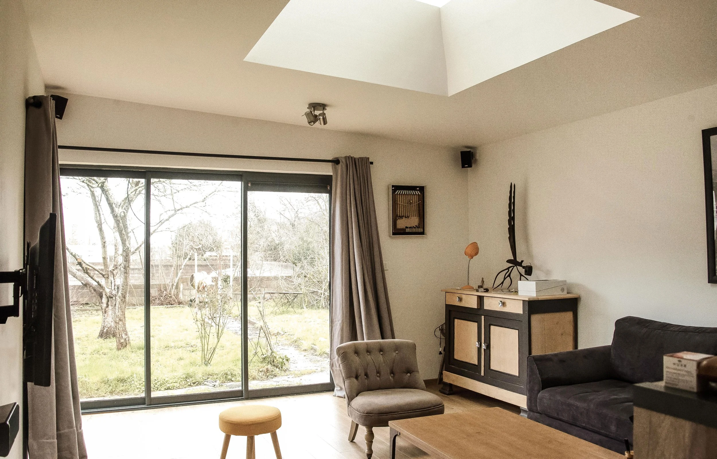 Intérieur d'un salon avec un grand vitrage donnant sur un jardin, mobilier moderne et décorations variées.