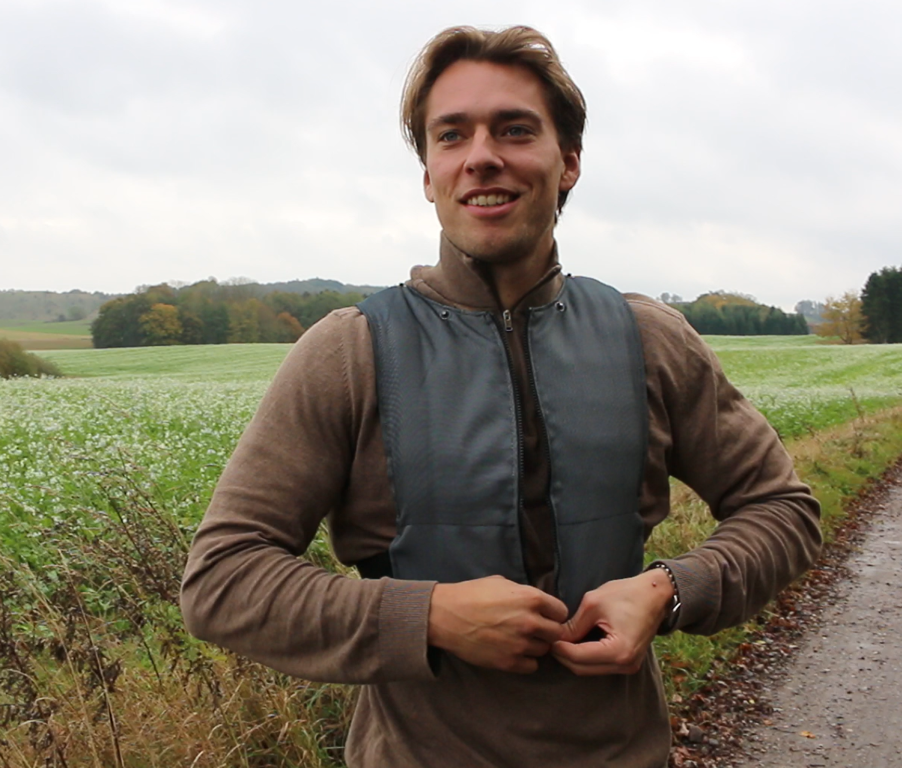 Young man smiling outdoors in a field with greenery and trees in the background, wearing a Vrang Vision weighted vest.