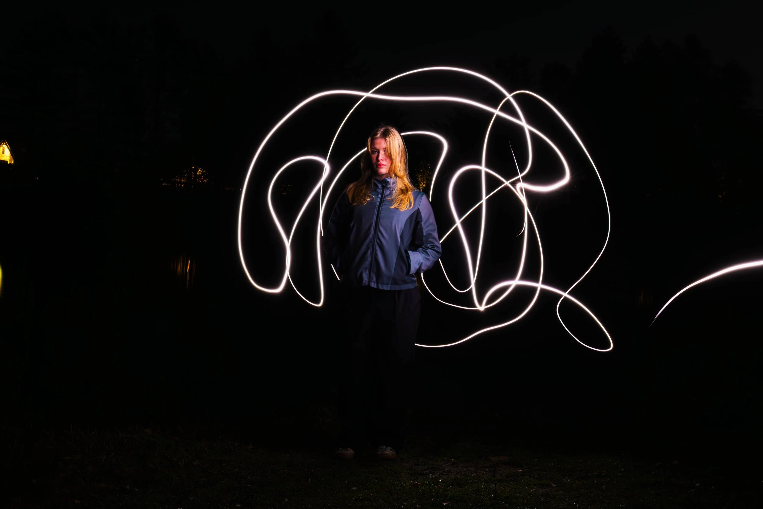 A woman standing outdoors at night with light trails swirling around her, created by long exposure photography.