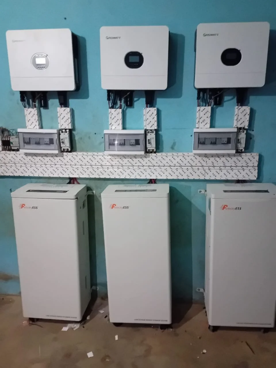 Installation de trois onduleurs solaires et de leur équipement de distribution électrique sur un mur turquoise.