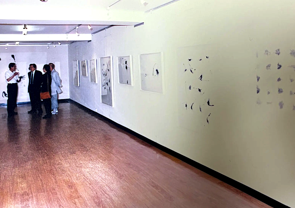 People viewing artwork in a gallery with white walls and wooden floor.