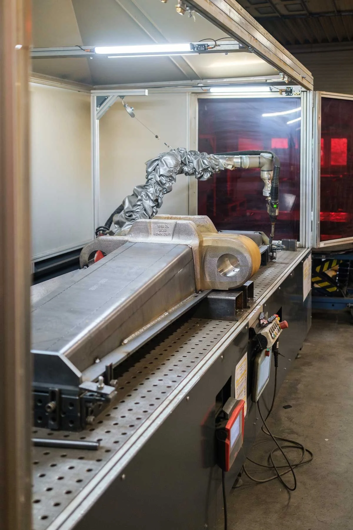 Ein industrieller Roboterarm in einer geschlossenen Arbeitsumgebung, die mit rot leuchtenden Sichtschutzfolien versehen ist, steht auf einer Metallarbeitsplatte.