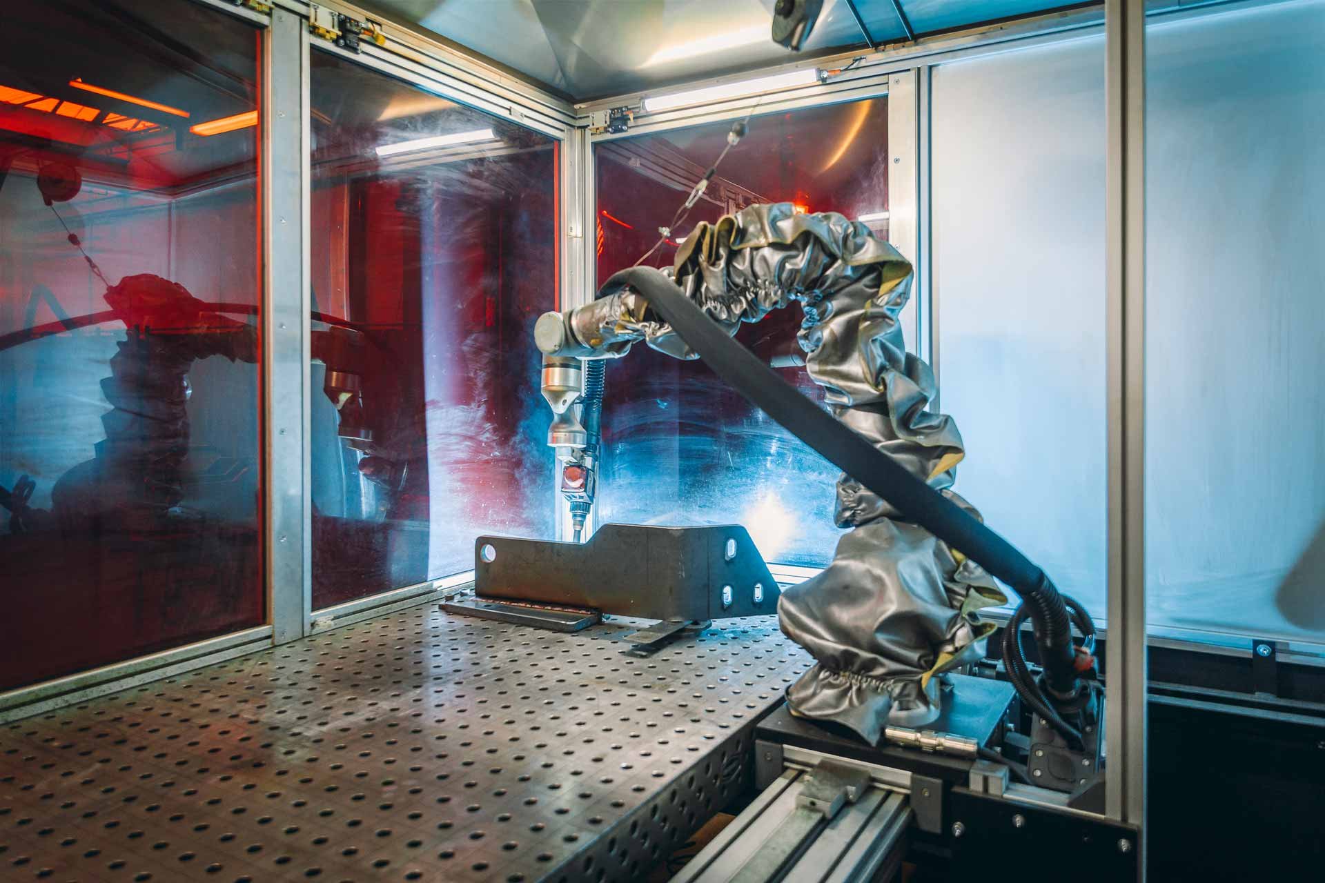 Industriereparatur oder -fertigung mit einem Roboterarm, der in einer abgeschirmten Kammer arbeitet, mit reflektierender Kleidung am Arm.