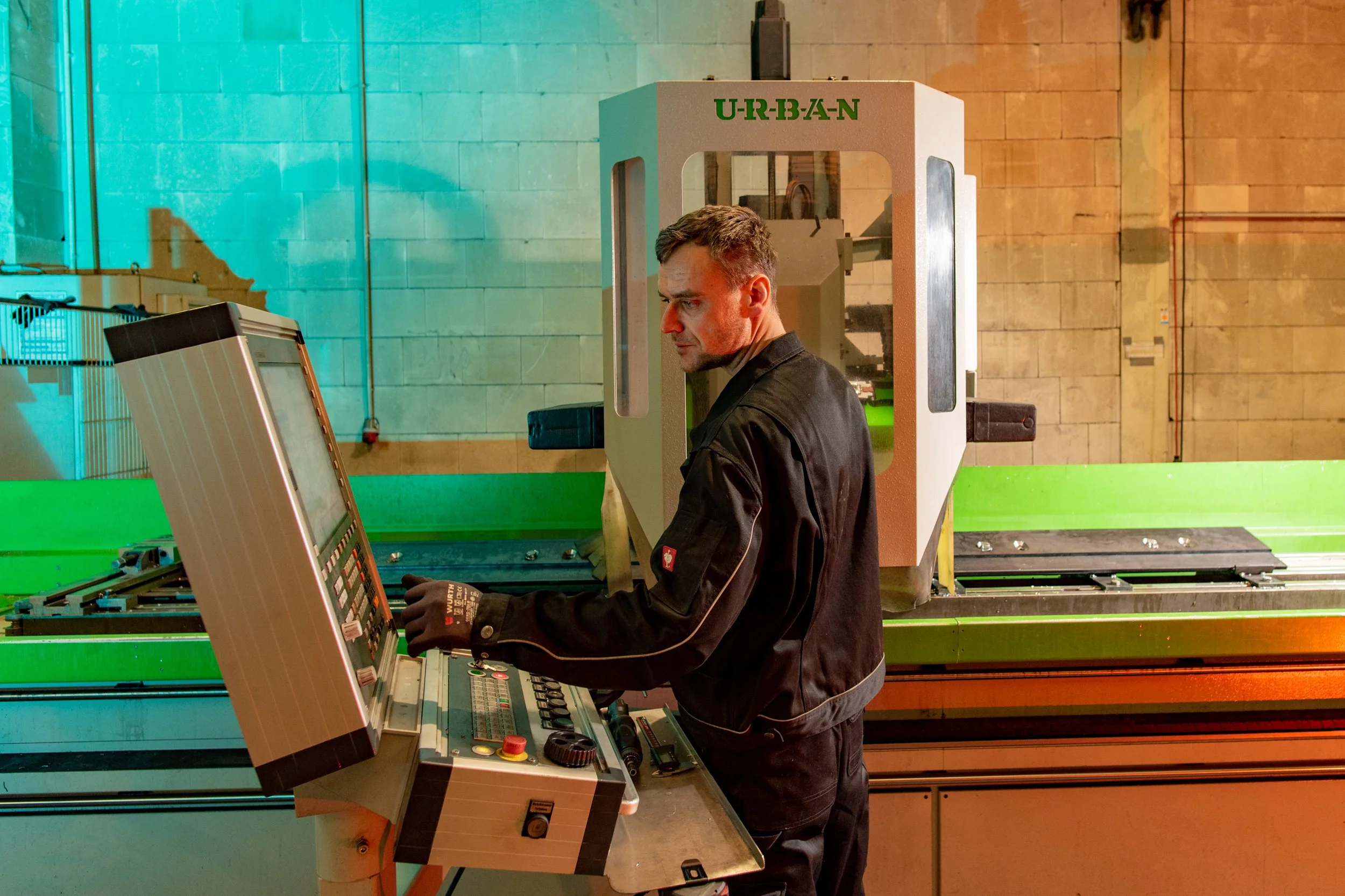 Mann in schwarzer Jacke arbeitet an einer CNC-Maschine in einer Werkshalle mit grauen Ziegelwänden.