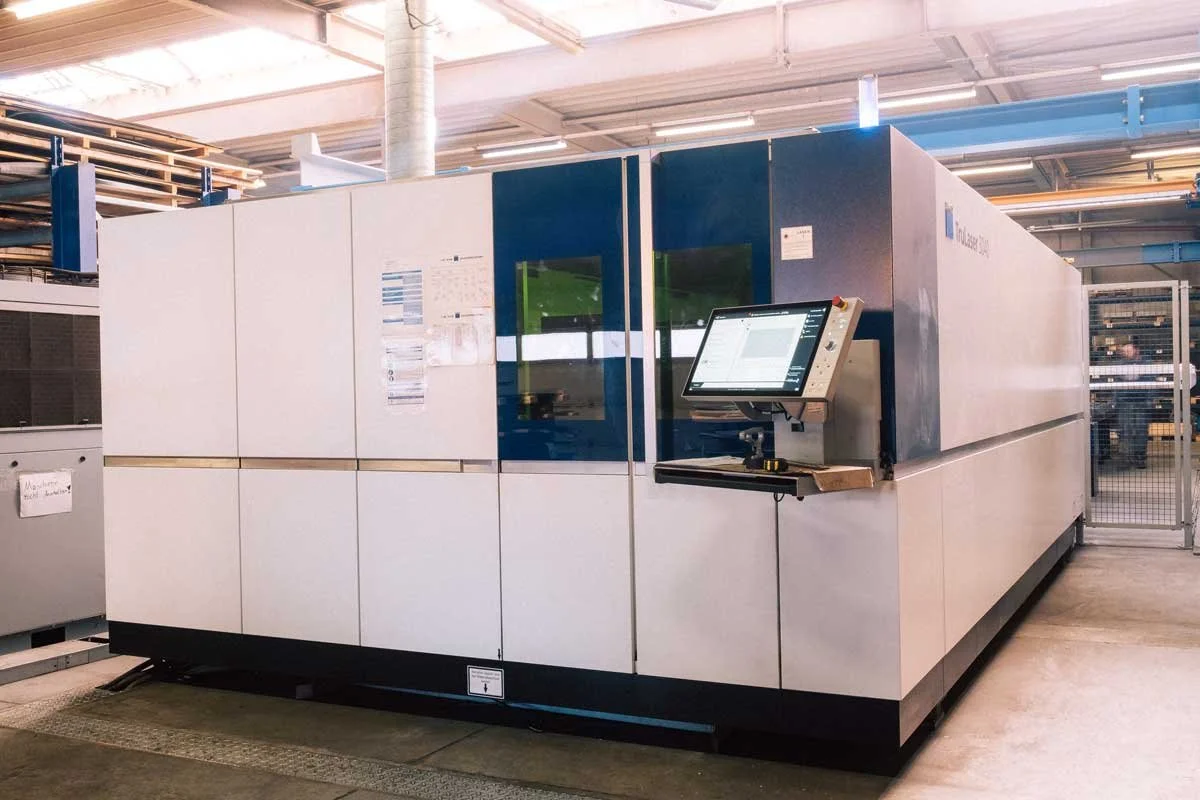 Großes industrielles 3D-Druckergerät in einer Fabrikhalle, mit einem Kontrollmonitor an der Seite.