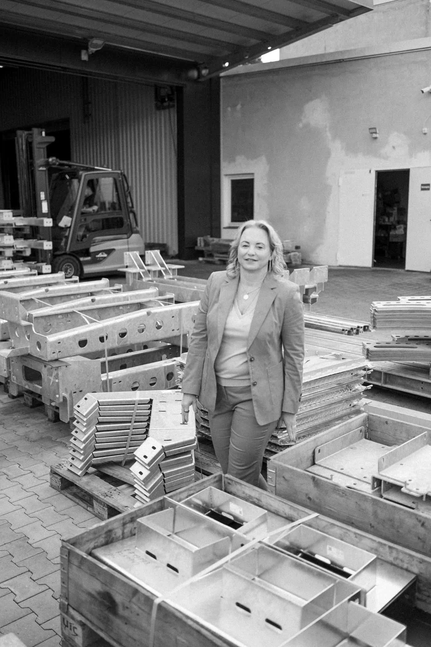 Eine Frau in einem Anzug, die in einem Lagerraum voller Metallteile steht.