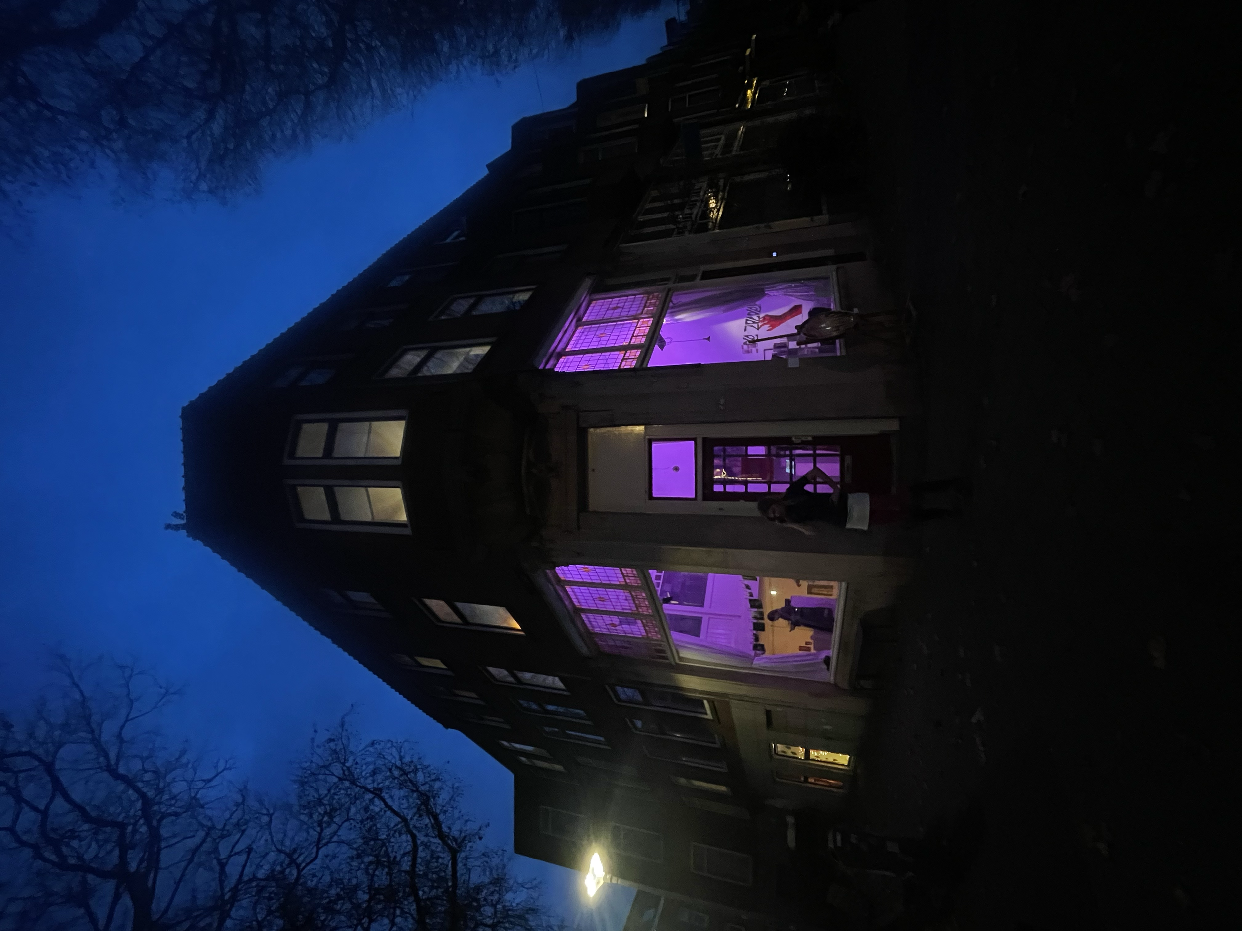 A multi-story residential building at night with purple and yellow lighting visible through the windows.
