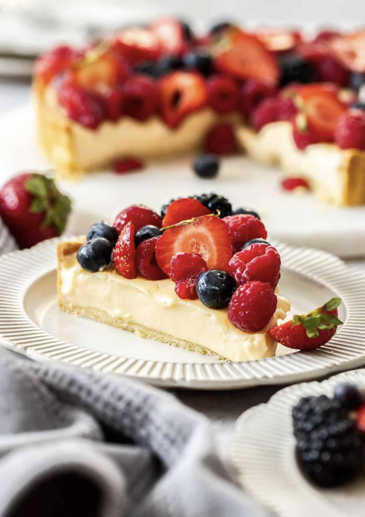 Custard tart topped with mixed berries including strawberries, blueberries, raspberries, and blackberries.