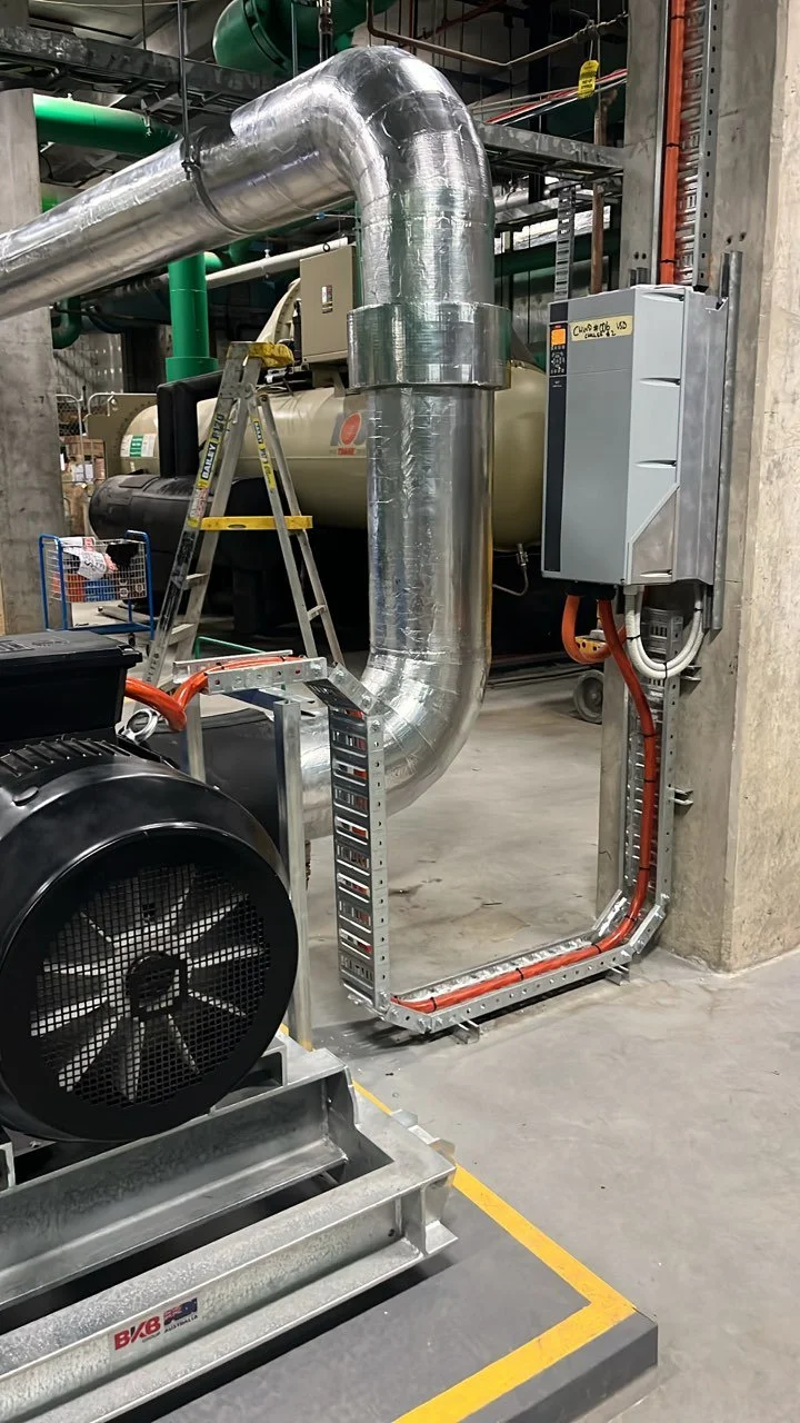 Industrial equipment with large silver insulated piping, a motor, and electrical panels in a factory or industrial setting.