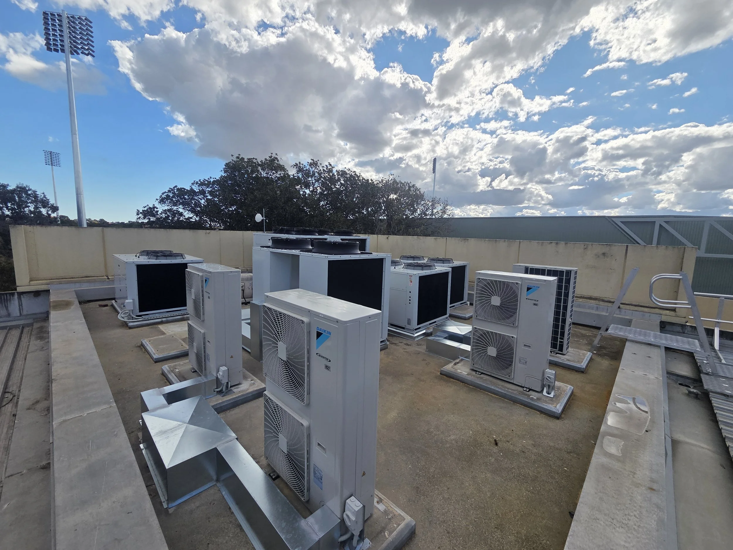 HVAC units on the rooftop of a building with a cloudy sky and trees in the background.