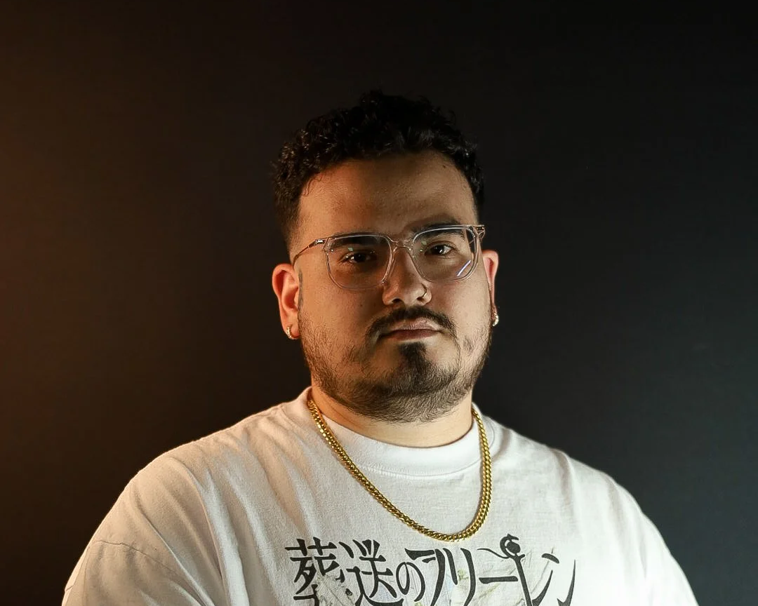 Man with beard, glasses, and gold chain wearing a white graphic t-shirt