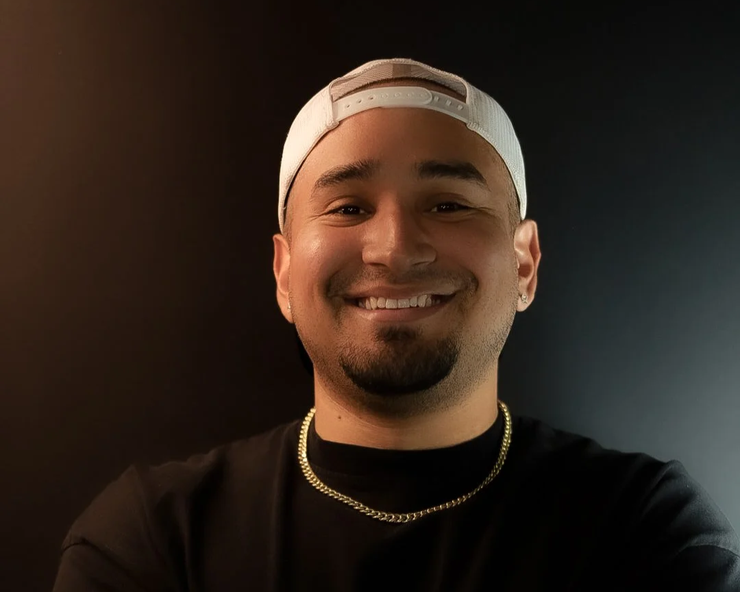 Man with goatee and white snapback hat wearing a gold chain in black shirt