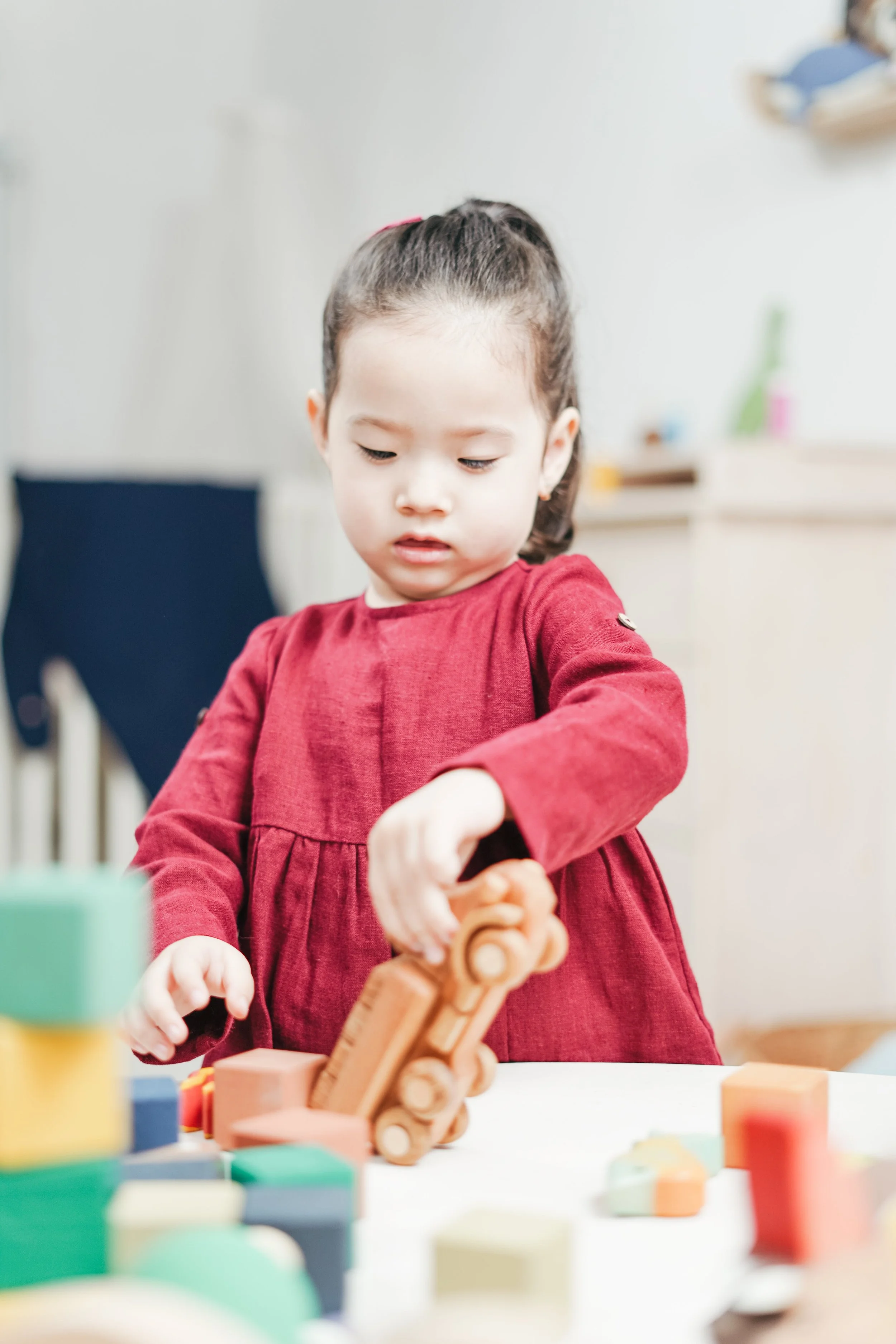 little girl with a pony tail, playing with wooden truck