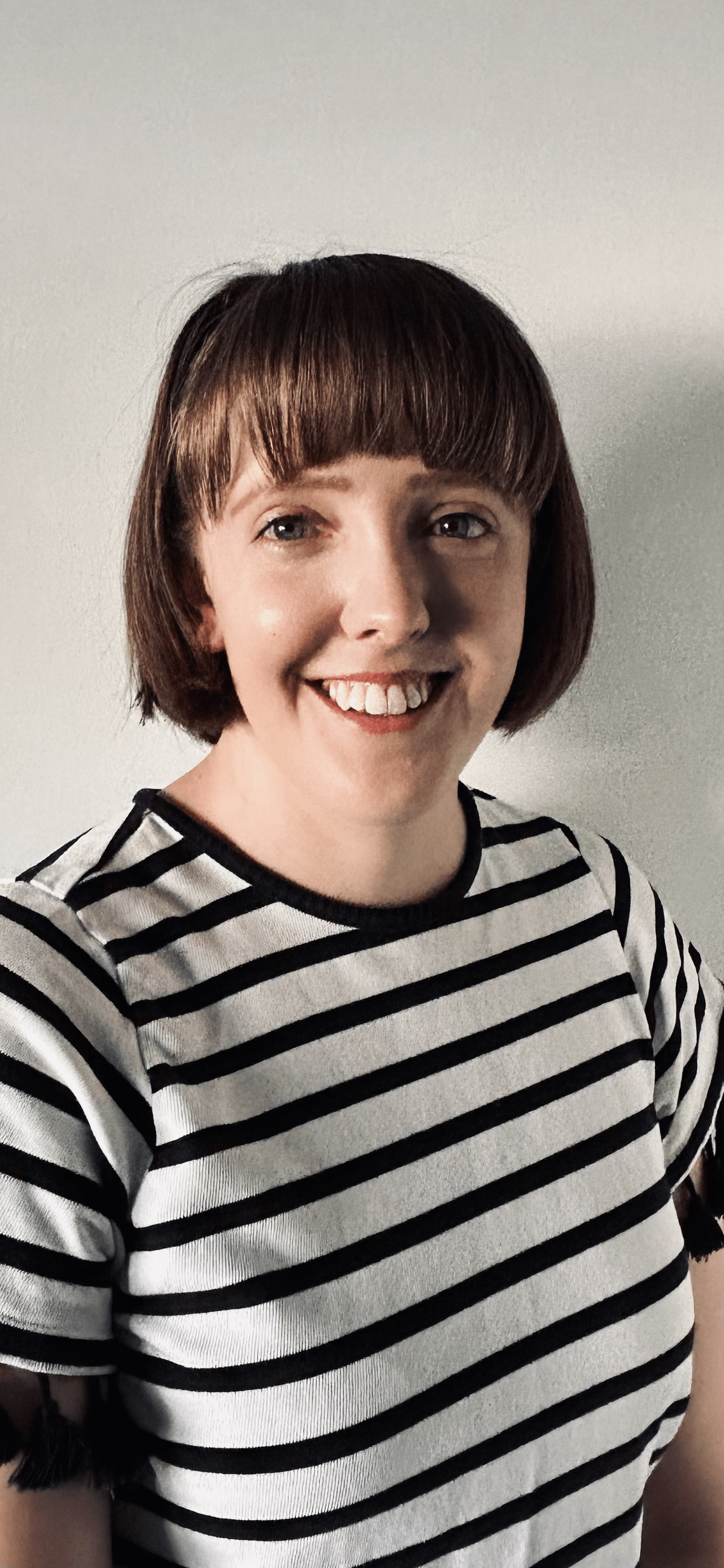 Photo of a woman with a fringe, smiling. She is wearing a black and white striped top.